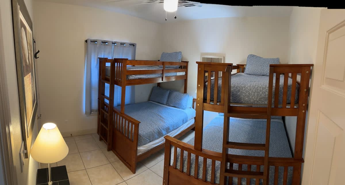 Another view of the children's bedroom, showcasing two sturdy wooden bunk beds with blue and white patterned bedding. A floor lamp stands in the corner, and a window with blue curtains provides natural light.