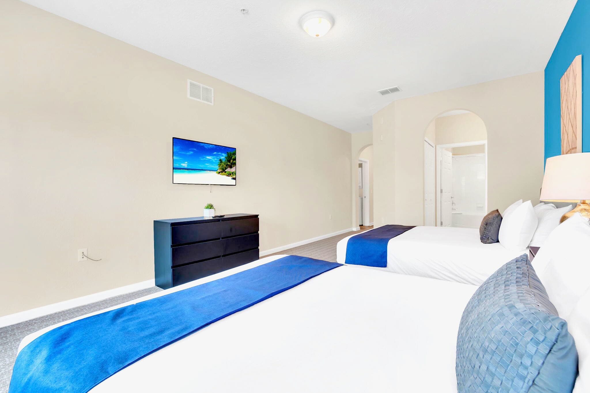 A wider view of the second bedroom shows the two queen beds, a black dresser with a wall-mounted TV, and an arched doorway leading to an adjacent bathroom.