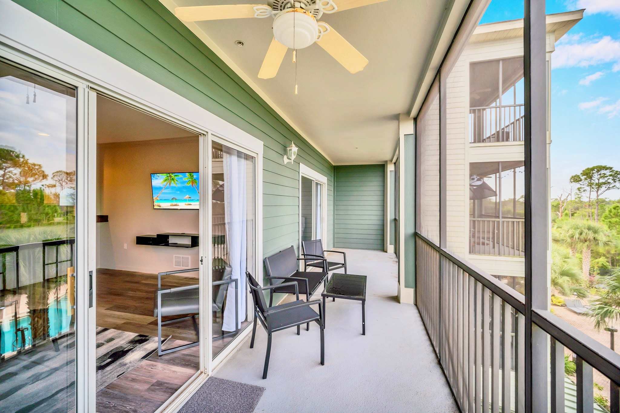 Wide screened balcony with black outdoor furniture, including chairs and a table, accessible via sliding glass doors from the interior, overlooking a natural landscape.