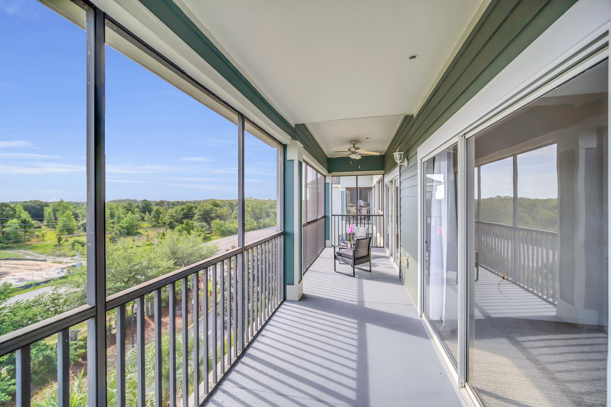 A long, screened-in balcony extends along the side of the building, featuring outdoor seating at one end and offering expansive views of the surrounding landscape and a construction area.