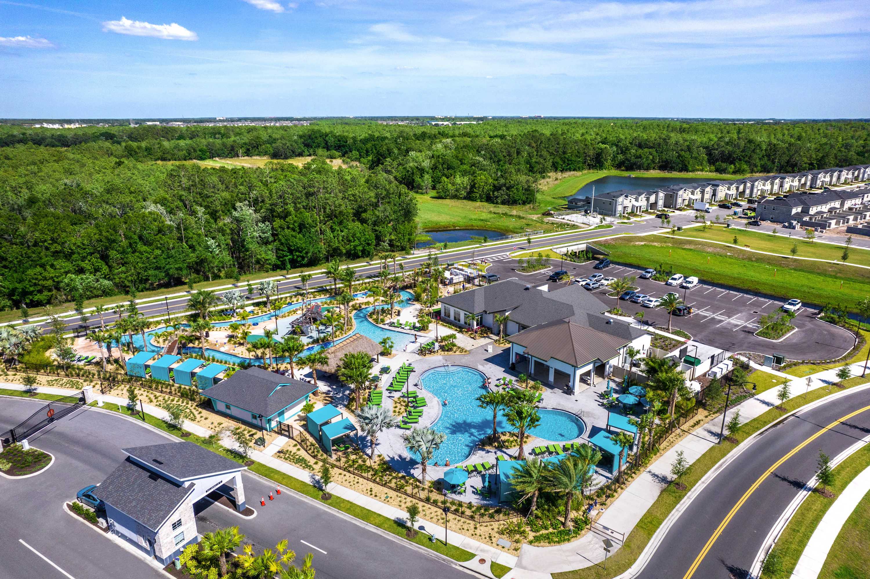 An aerial view showcases a large community water park area with multiple swimming pools, a lazy river, cabanas, and lounge chairs, surrounded by lush greenery and residential buildings.