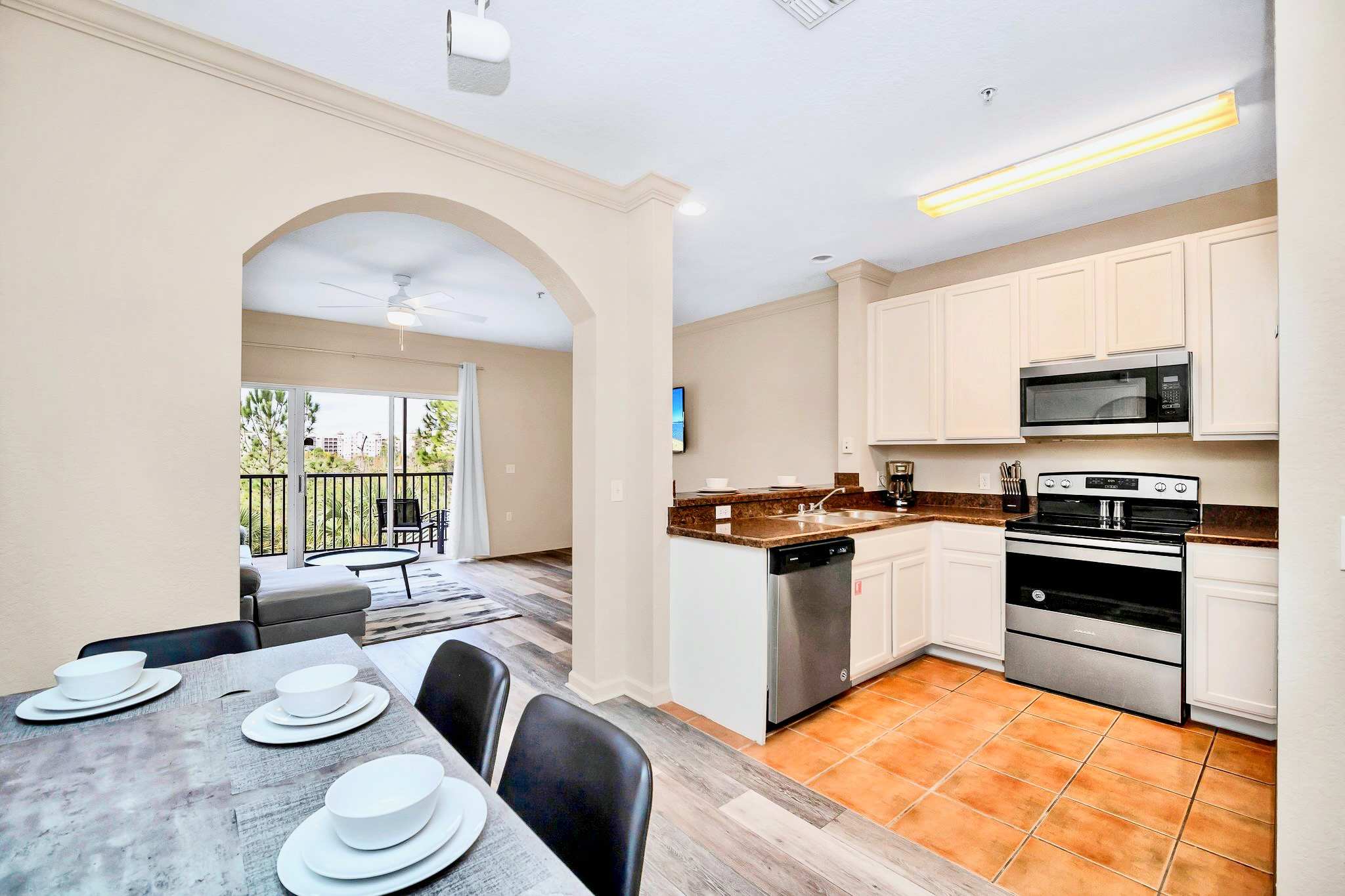 Well-equipped kitchen featuring light cream cabinetry, granite countertops, stainless steel appliances including a range, microwave, and dishwasher, with terracotta-colored tile flooring.