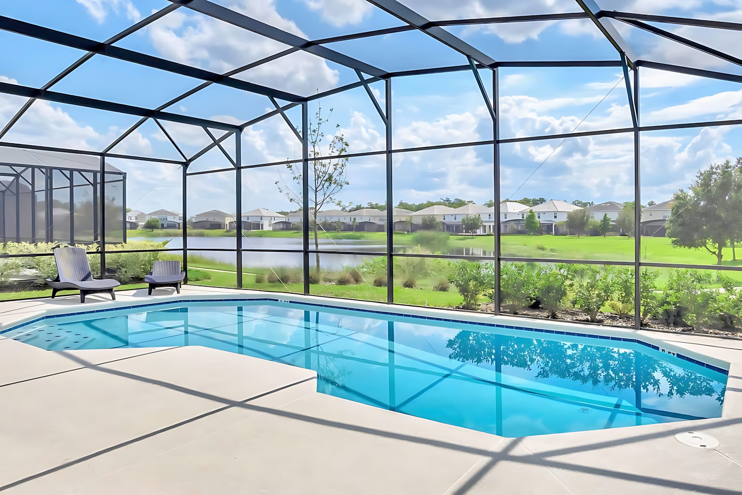 A screened-in private pool with clear blue water and two lounge chairs offers a tranquil view of a lake and distant houses. The enclosure provides an open feel while protecting from insects.
