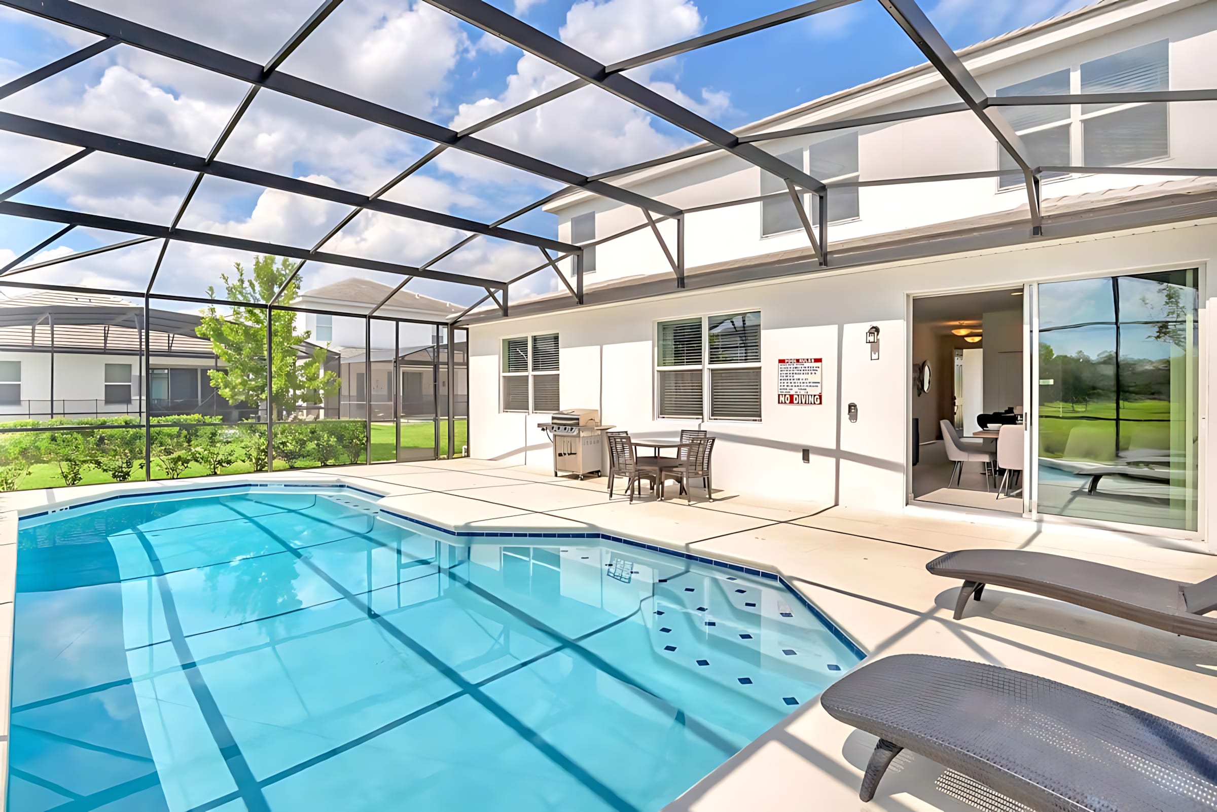 The back exterior of the house features a screened-in private pool and patio area, complete with a BBQ grill and an outdoor dining set. Sliding glass doors connect the pool deck to the interior, offering views of the lake and neighboring properties.