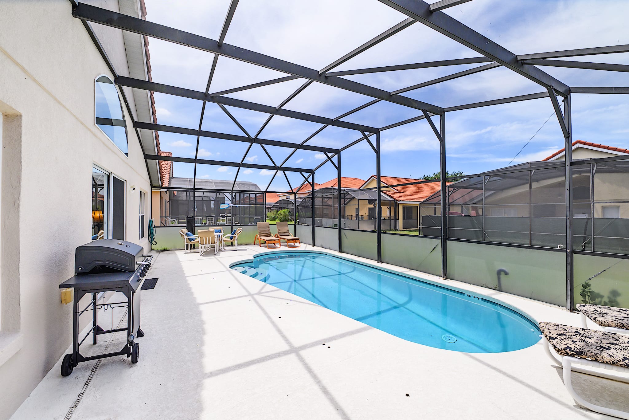 Screened-in private pool area with a rectangular pool, two lounge chairs, a BBQ grill, and an outdoor dining set, all on a light concrete deck.