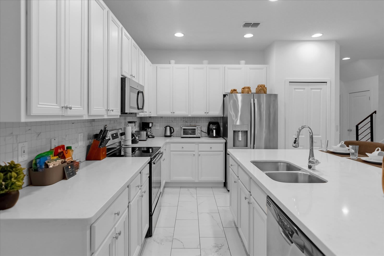 Well-equipped modern kitchen featuring white shaker cabinets, white quartz countertops, stainless steel appliances including a range and dishwasher, and a white subway tile backsplash.