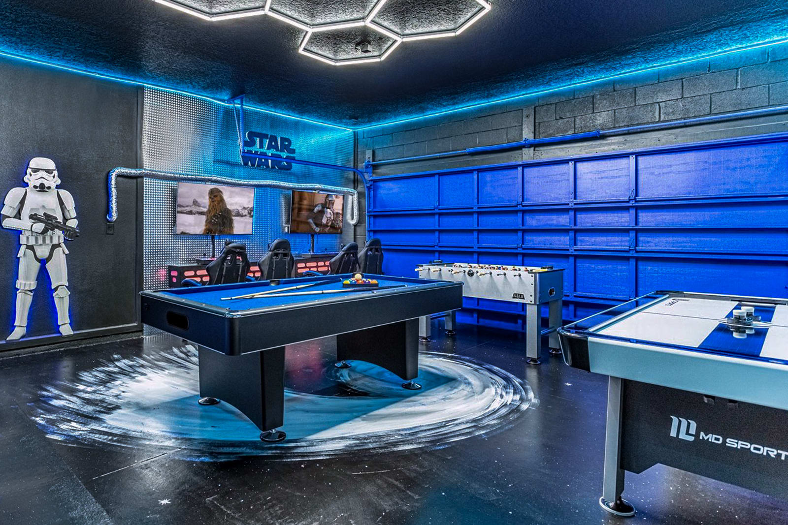 A vibrant Star Wars-themed game room featuring a blue-felt pool table, foosball, and air hockey table, all illuminated by blue LED lighting and a hexagonal ceiling light, with a life-sized Stormtrooper figure.