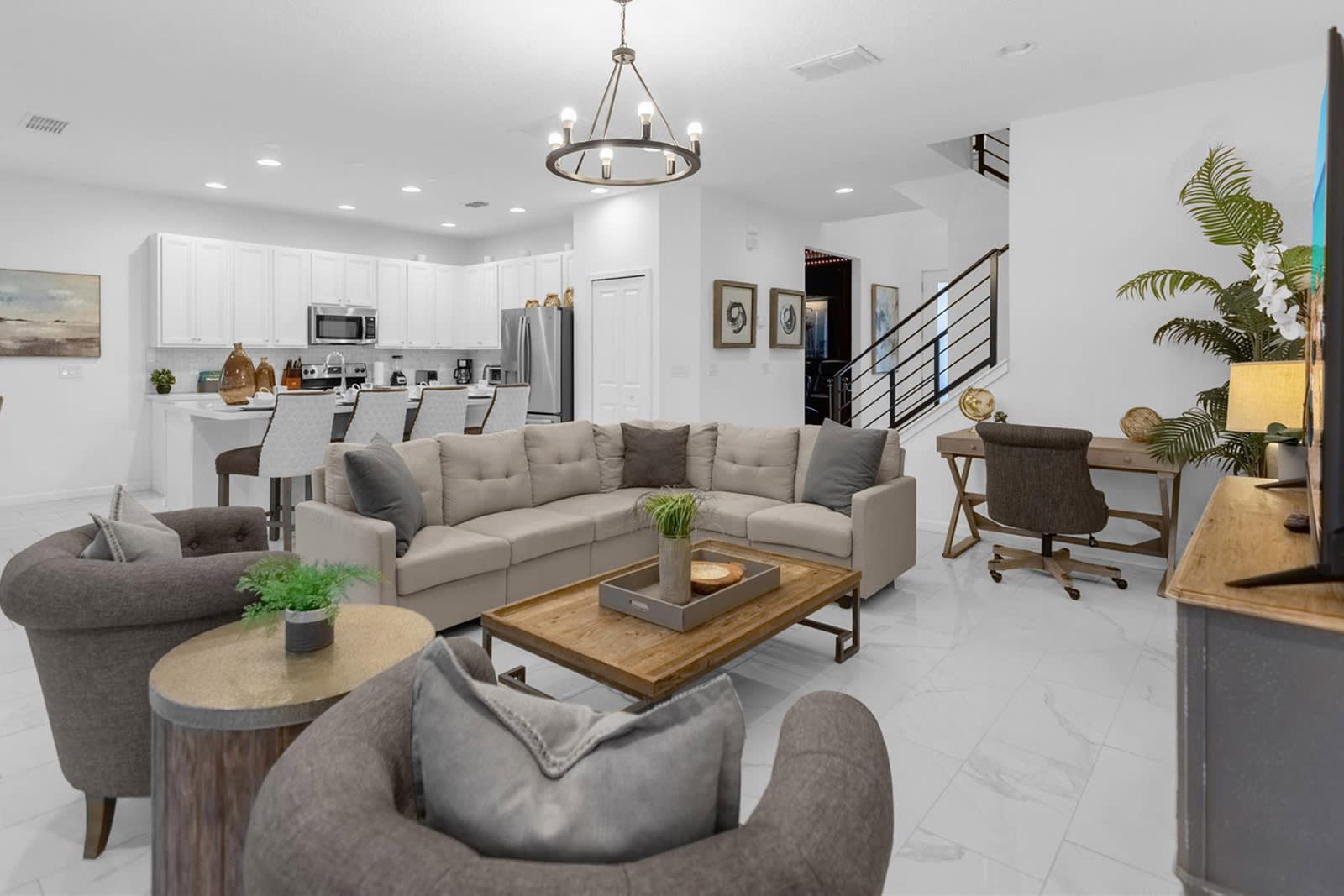Bright and open-concept living room with a large L-shaped sectional sofa, two armchairs, a wooden coffee table, and a view towards the modern white kitchen and a staircase.