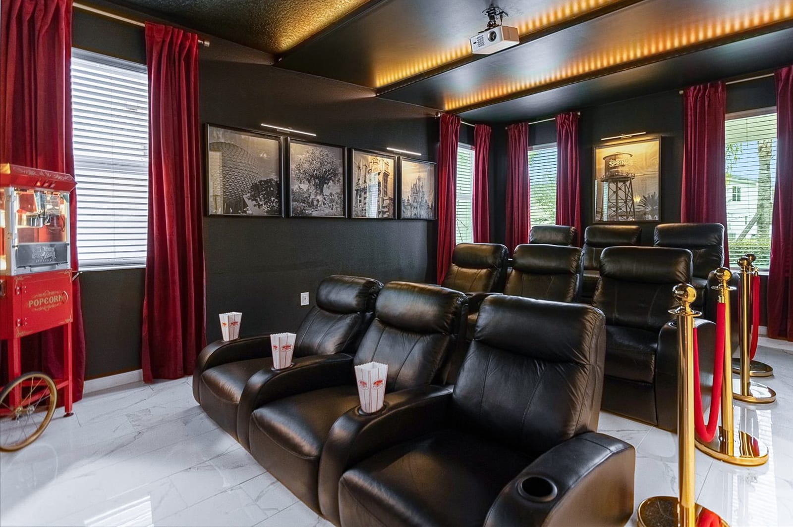 A spacious home cinema room with several rows of black leather recliners, red velvet curtains, a large projection screen, and a vintage red popcorn machine, creating a classic movie theater ambiance.