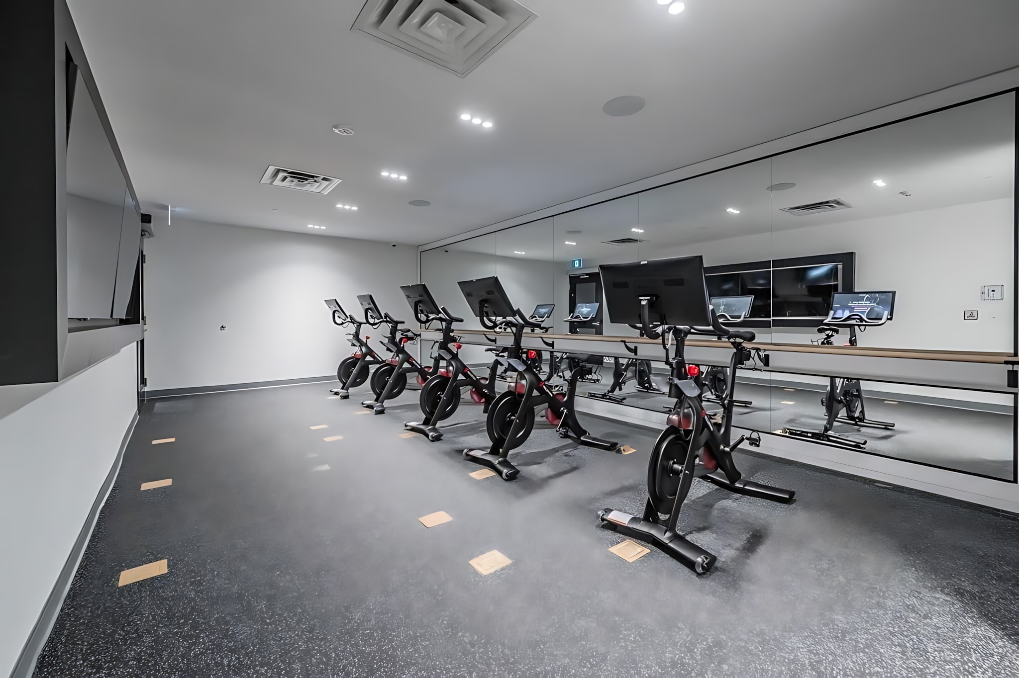 Dedicated spin studio within the fitness center, featuring multiple stationary bikes with screens, arranged in rows facing a large mirrored wall, with dark rubber flooring.
