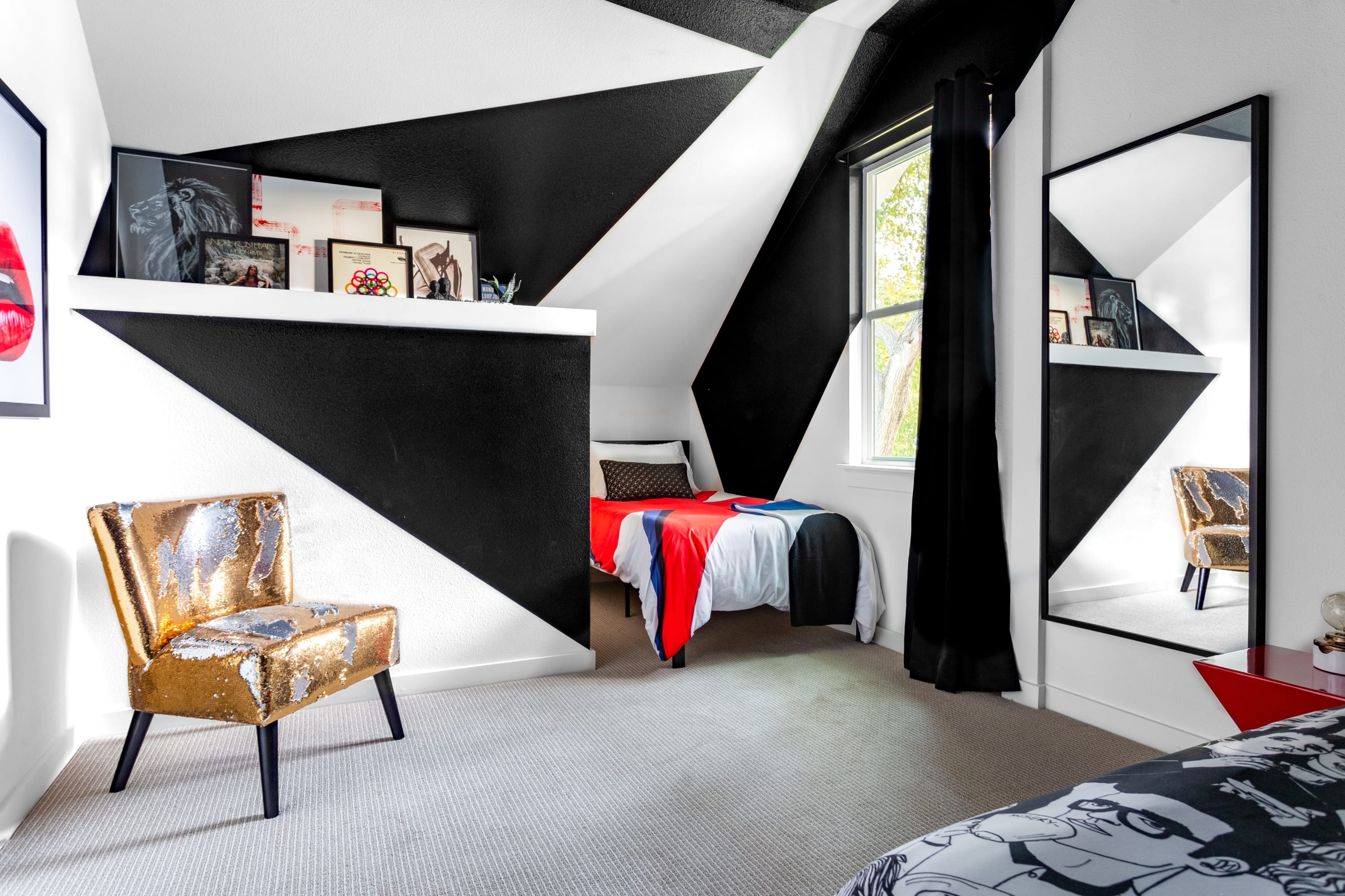 Playful bedroom with striking black and white geometric wall patterns, a single bed with red and black bedding, and a gold sequined chair.
