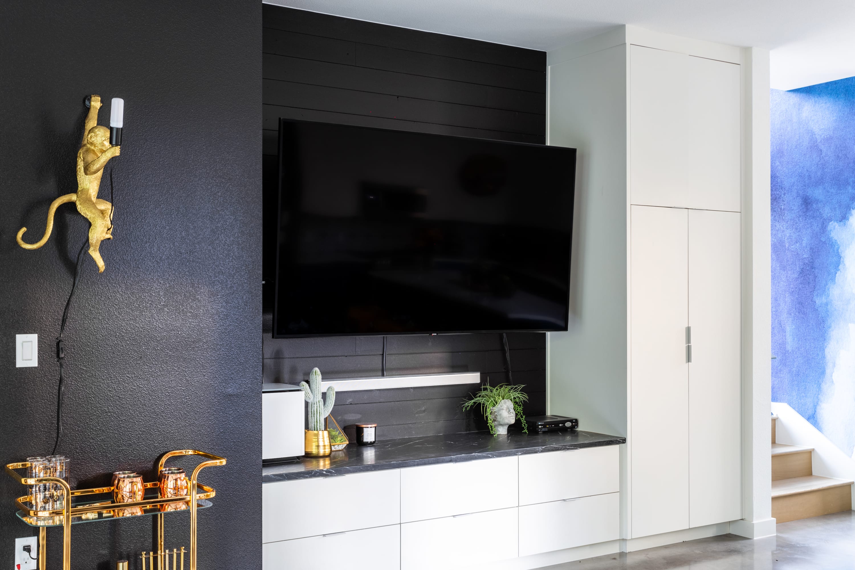 A sleek entertainment area features a wall-mounted TV above a black and white console, with a golden monkey sconce on a textured dark wall and white built-in cabinets.