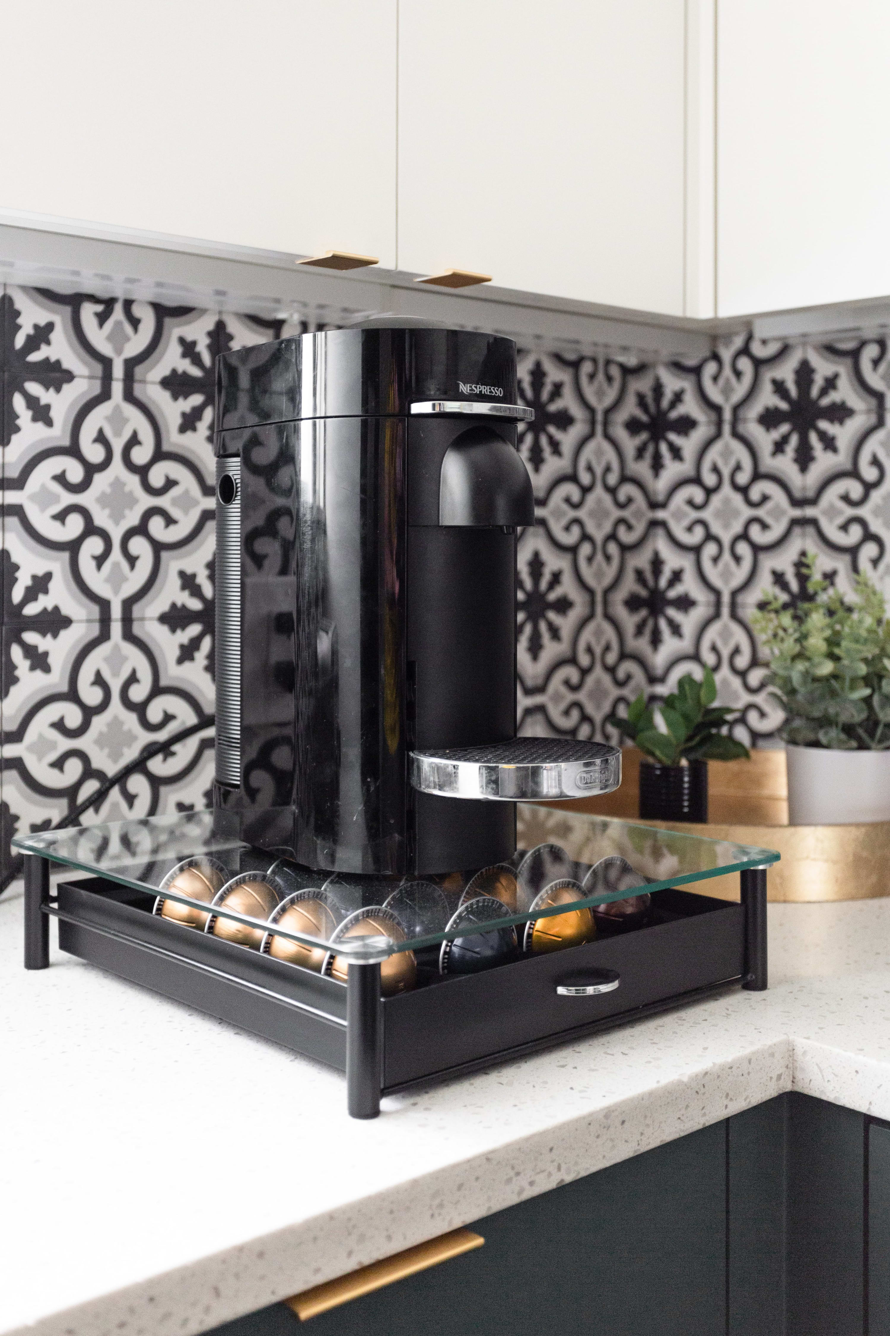 Close-up of a Nespresso coffee machine and capsule dispenser on a white speckled countertop, with a distinctive black and white patterned backsplash in the background.