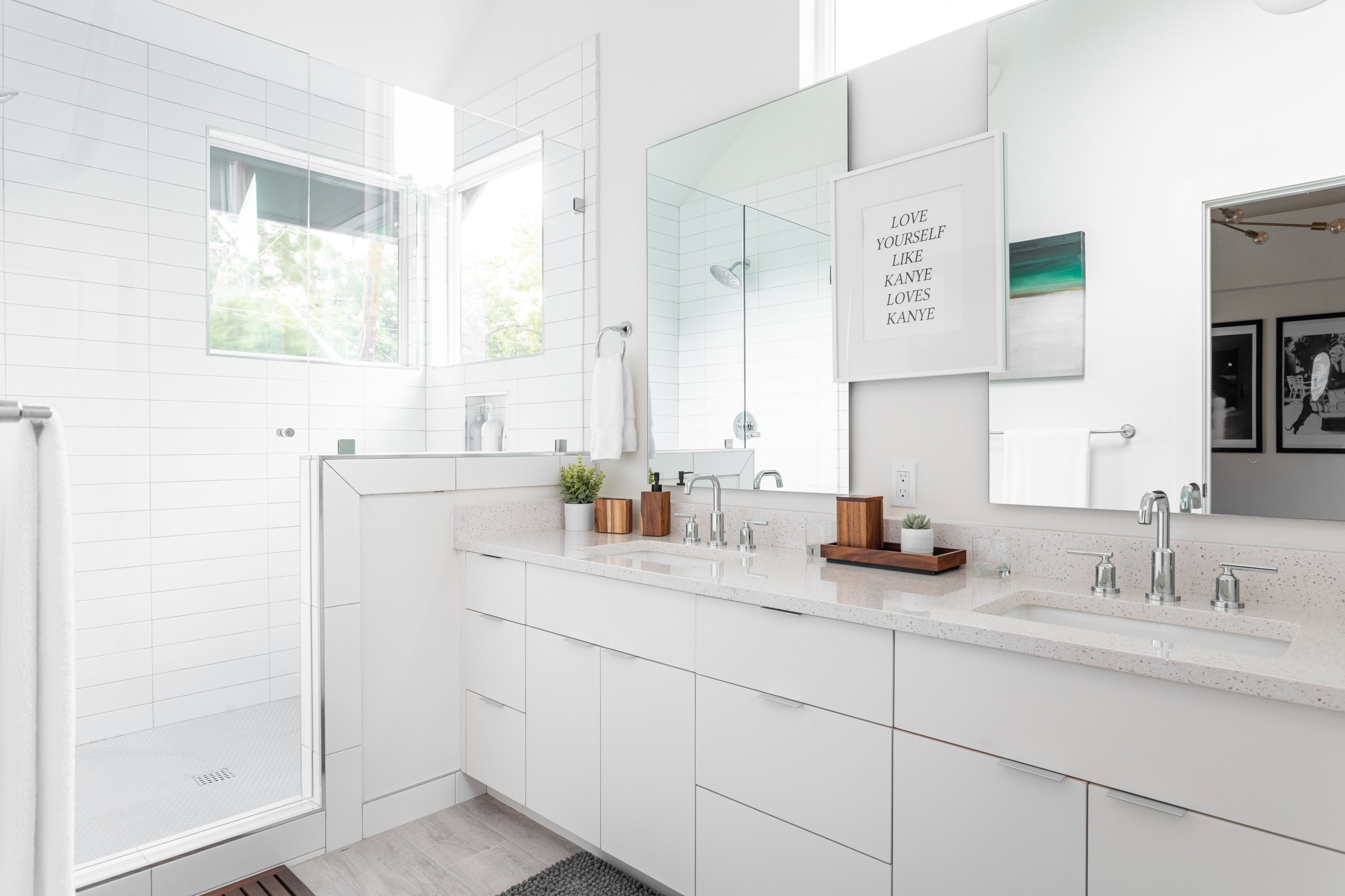 Bright, modern bathroom with a white double vanity, light speckled countertop, chrome faucets, and a large walk-in shower with white subway tiles and a window.