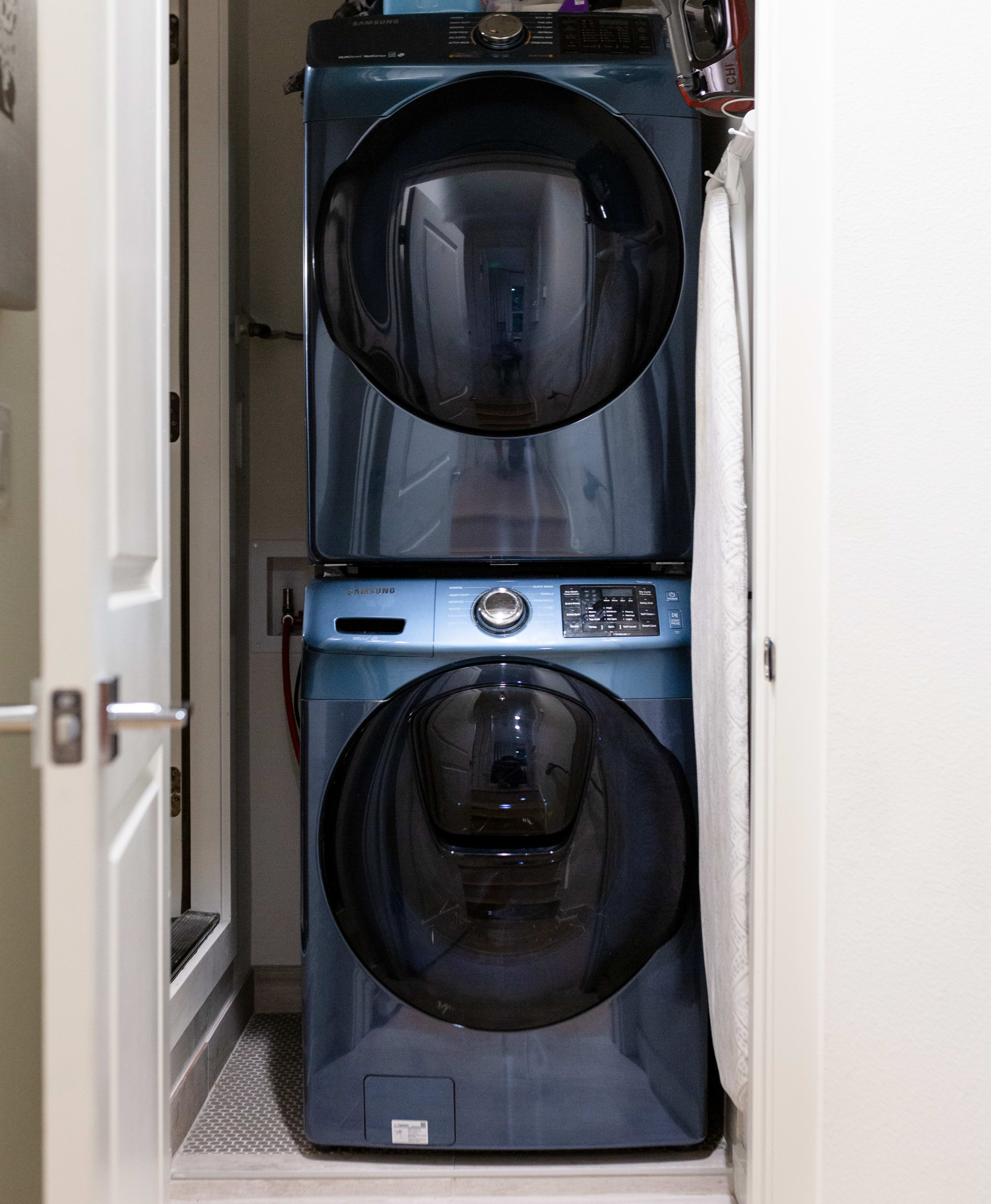 Compact laundry area featuring a modern blue stacked front-loading washer and dryer unit, neatly tucked into a closet space. The efficient setup is surrounded by white walls and a light-colored floor.