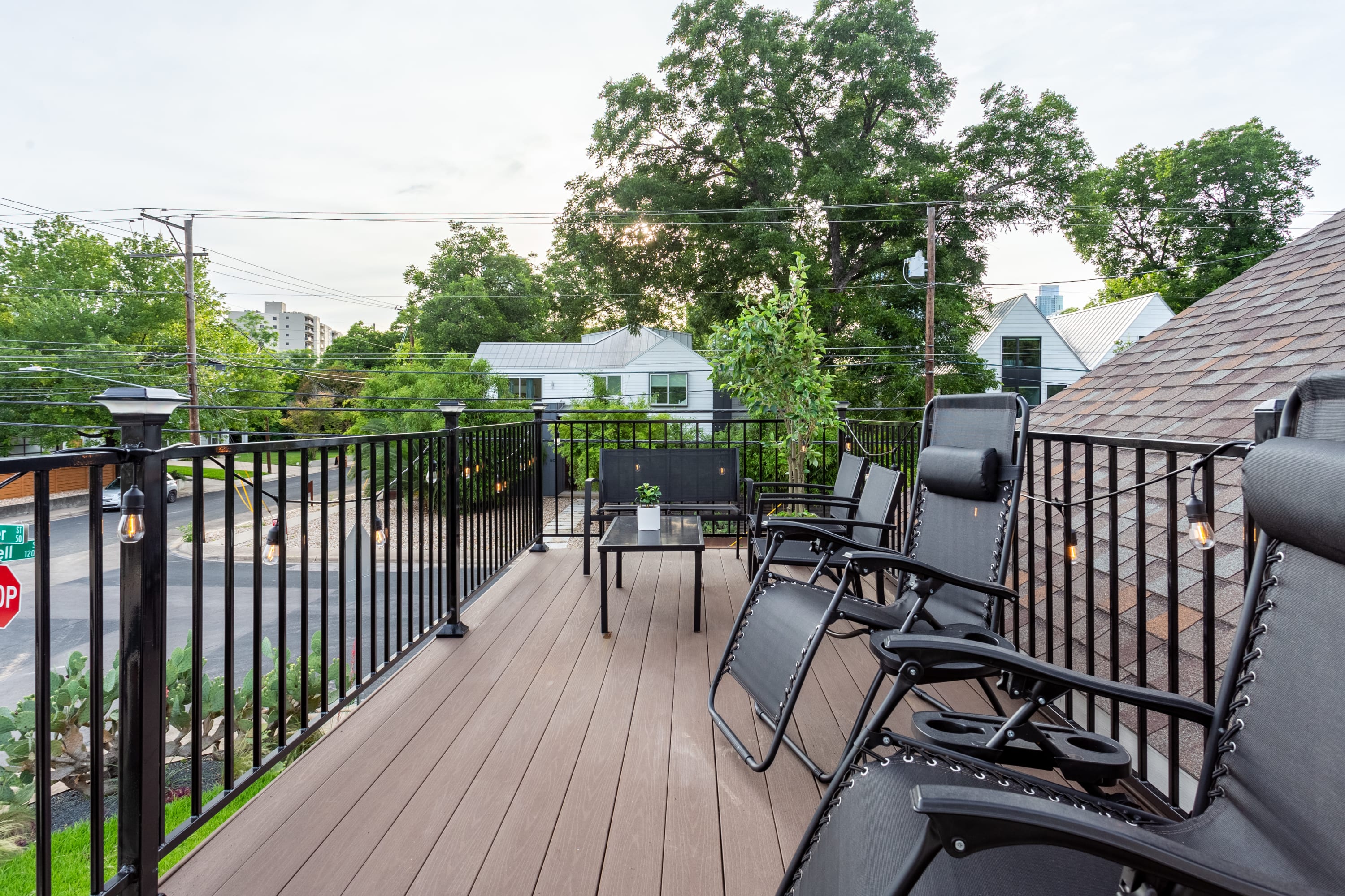 A spacious rooftop deck with dark composite decking offers multiple black zero-gravity lounge chairs and a small table, overlooking a tree-lined street and neighborhood.