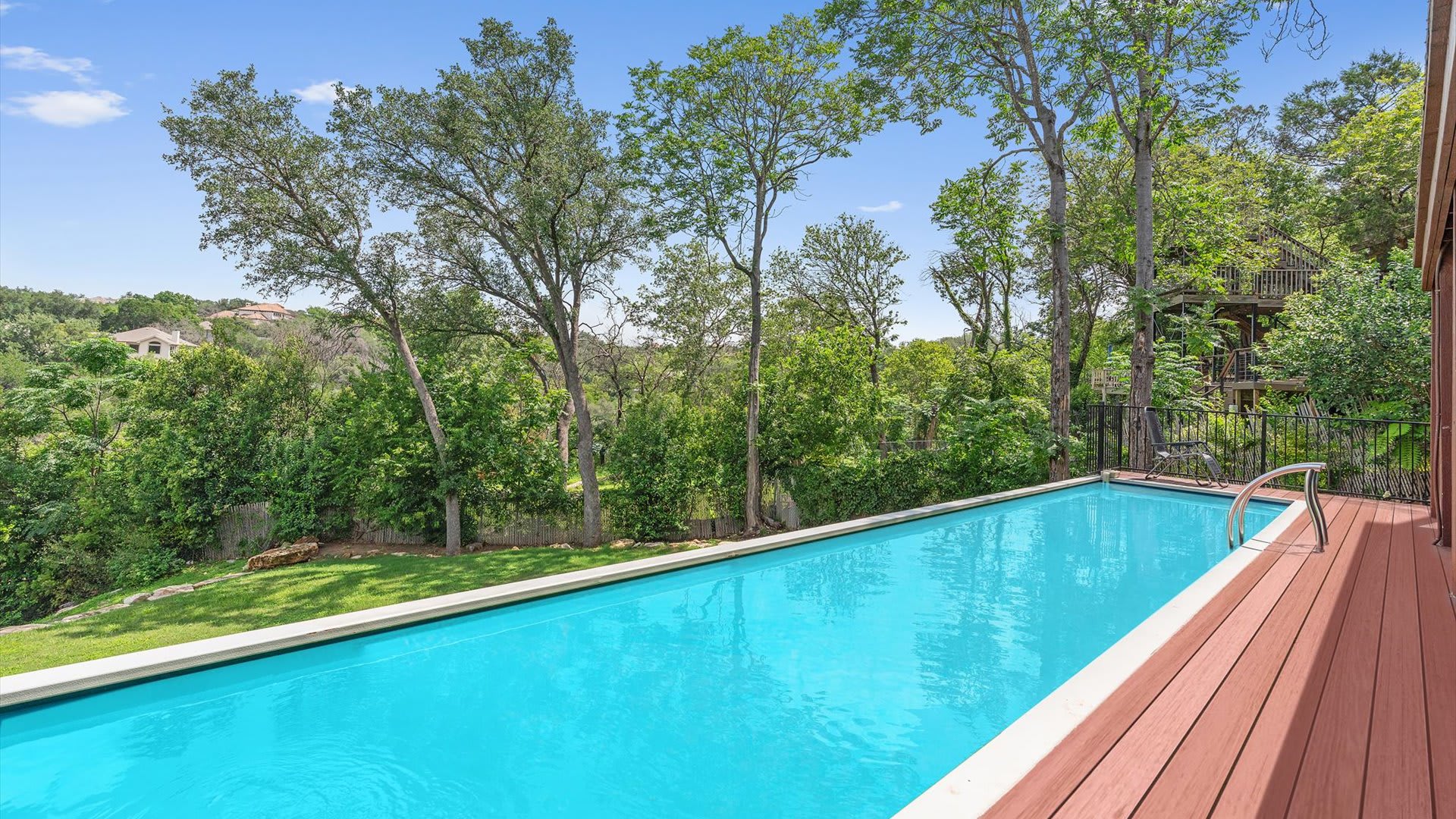 Serene outdoor swimming pool with a wooden deck, nestled amidst lush green trees and a grassy lawn, providing a private and tranquil setting.
