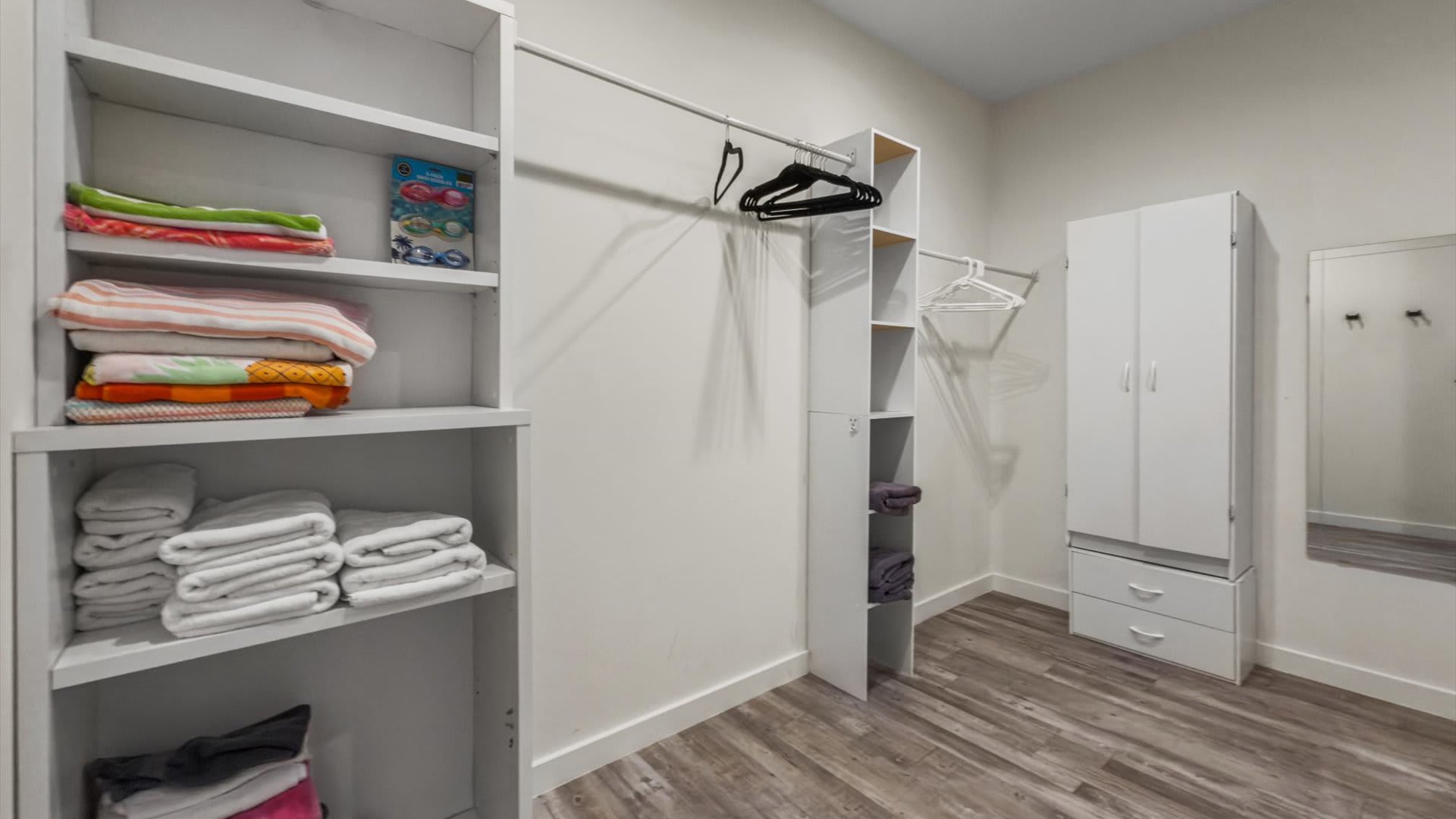 Another view of a well-organized walk-in closet, showcasing white shelving units filled with neatly folded towels and linens, along with hanging rods for clothes. The room has light wood-look flooring.