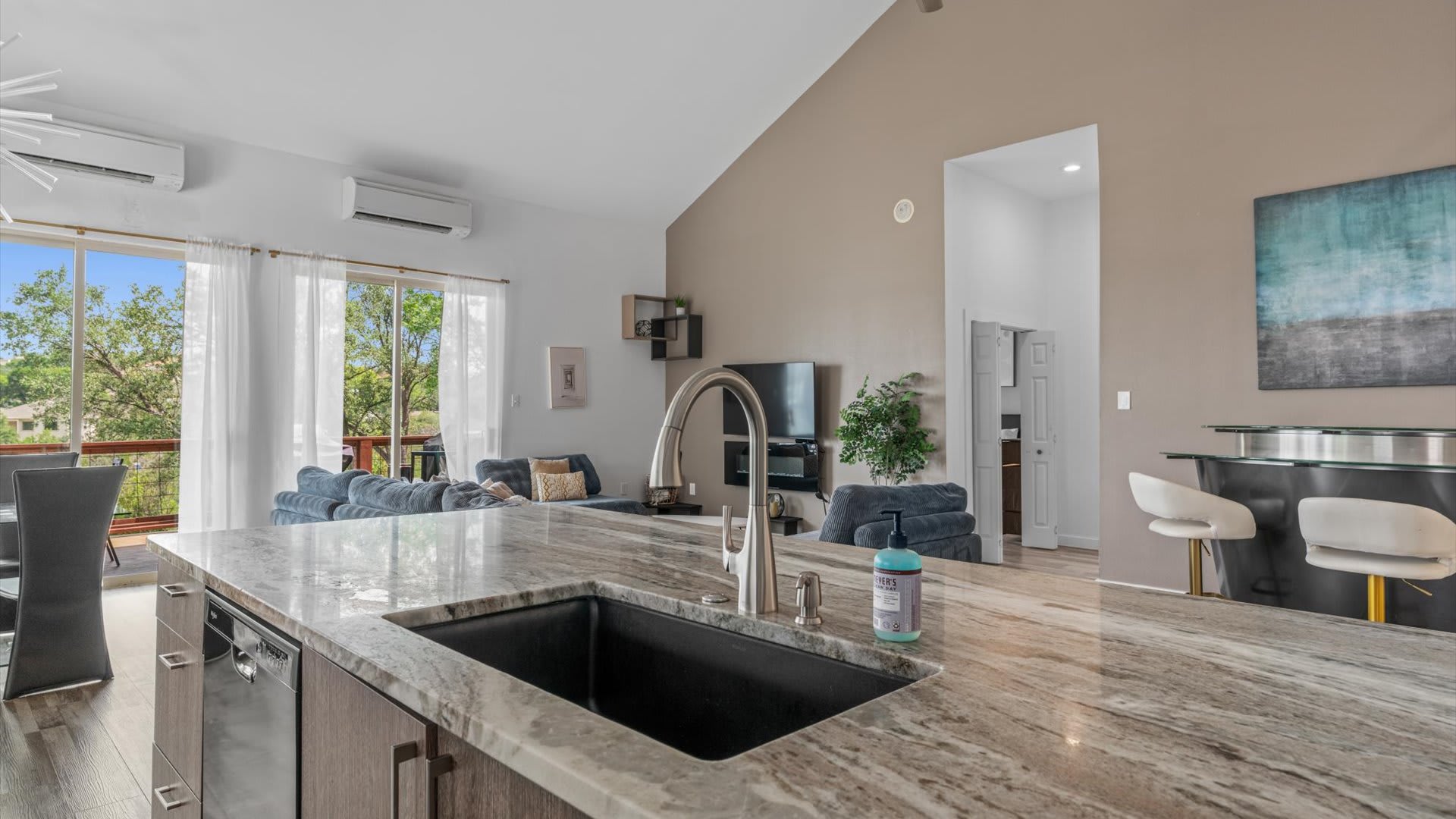 Close-up view of the kitchen island with a black sink and a modern faucet, featuring a light-colored granite countertop. The island also includes a dishwasher and bar seating on the opposite side.