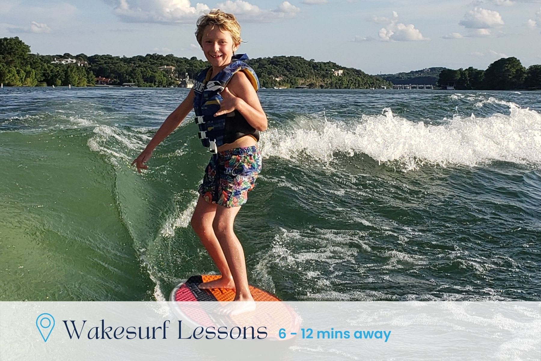 A young boy in a life vest is wakesurfing behind a boat on a wavy lake, giving a thumbs-up. The background shows a green, tree-lined shoreline under a partly cloudy sky, with text indicating 'Wakesurf Lessons 6 - 12 mins away'.