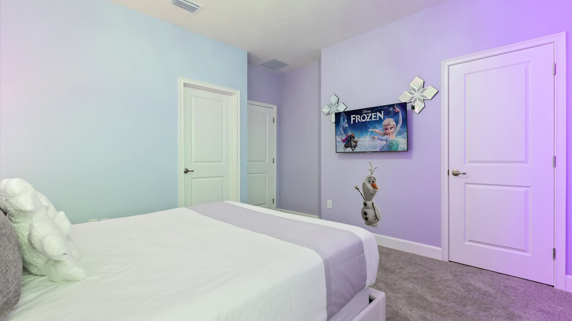Another view of the 'Frozen' themed bedroom, featuring a wall-mounted TV with 'Frozen' branding, a cutout of Olaf, and two white doors. The room has light purple walls and a grey carpet.