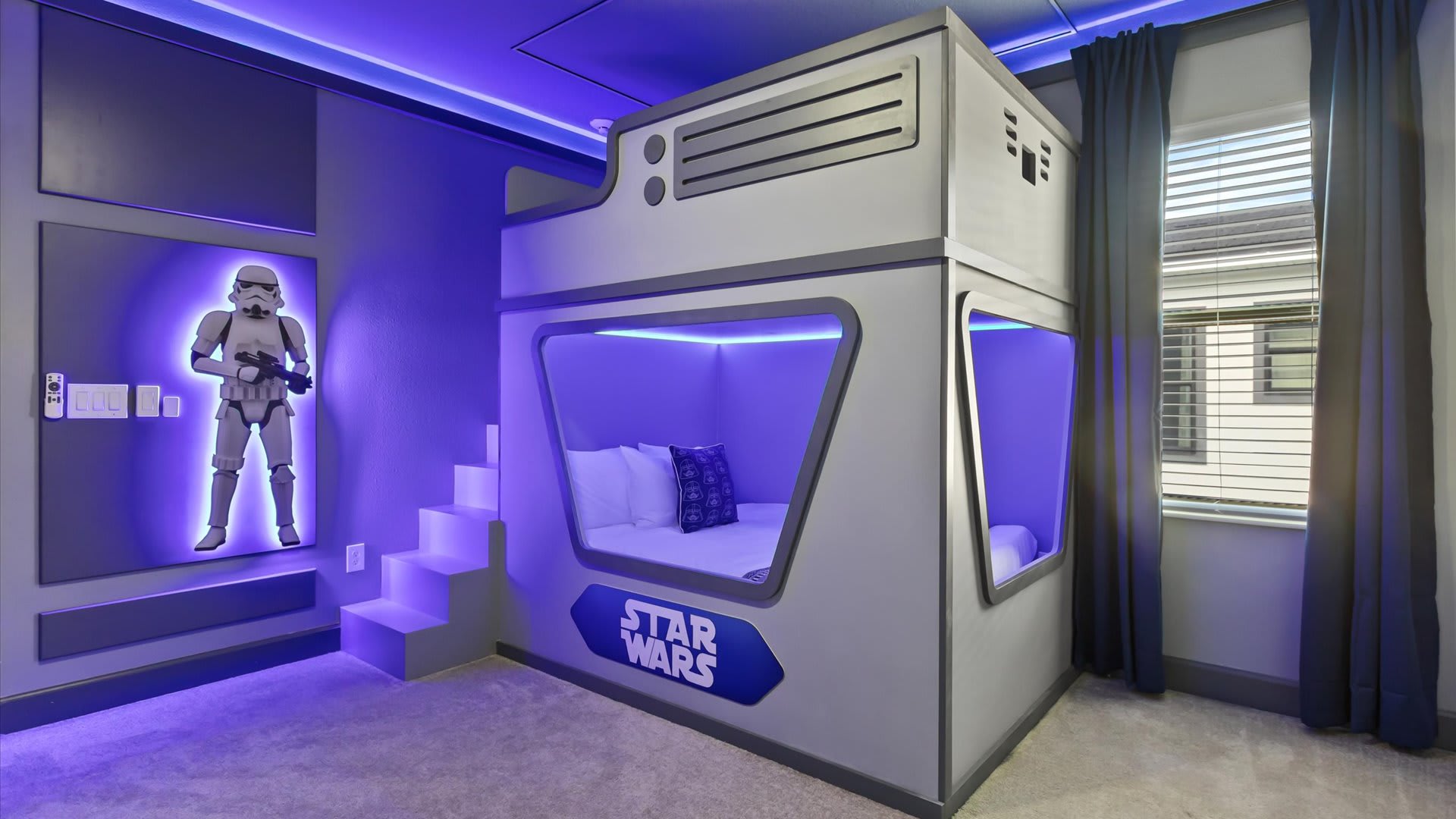 Star Wars themed bedroom featuring a custom-built bunk bed designed like a spaceship, illuminated with blue LED lighting. A large Stormtrooper wall decal adds to the immersive gray-walled space.