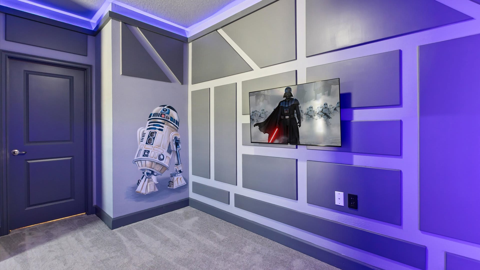 Another view of the Star Wars themed bedroom, showcasing a wall-mounted TV displaying Darth Vader, an R2-D2 wall decal, and geometric gray wall panels with subtle blue LED accent lighting.
