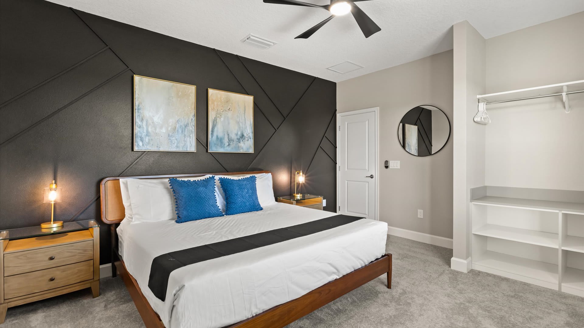 Stylish bedroom with a queen-sized bed, two wooden nightstands with gold lamps, and a striking black accent wall with geometric paneling. A built-in closet with shelving is visible on the right.