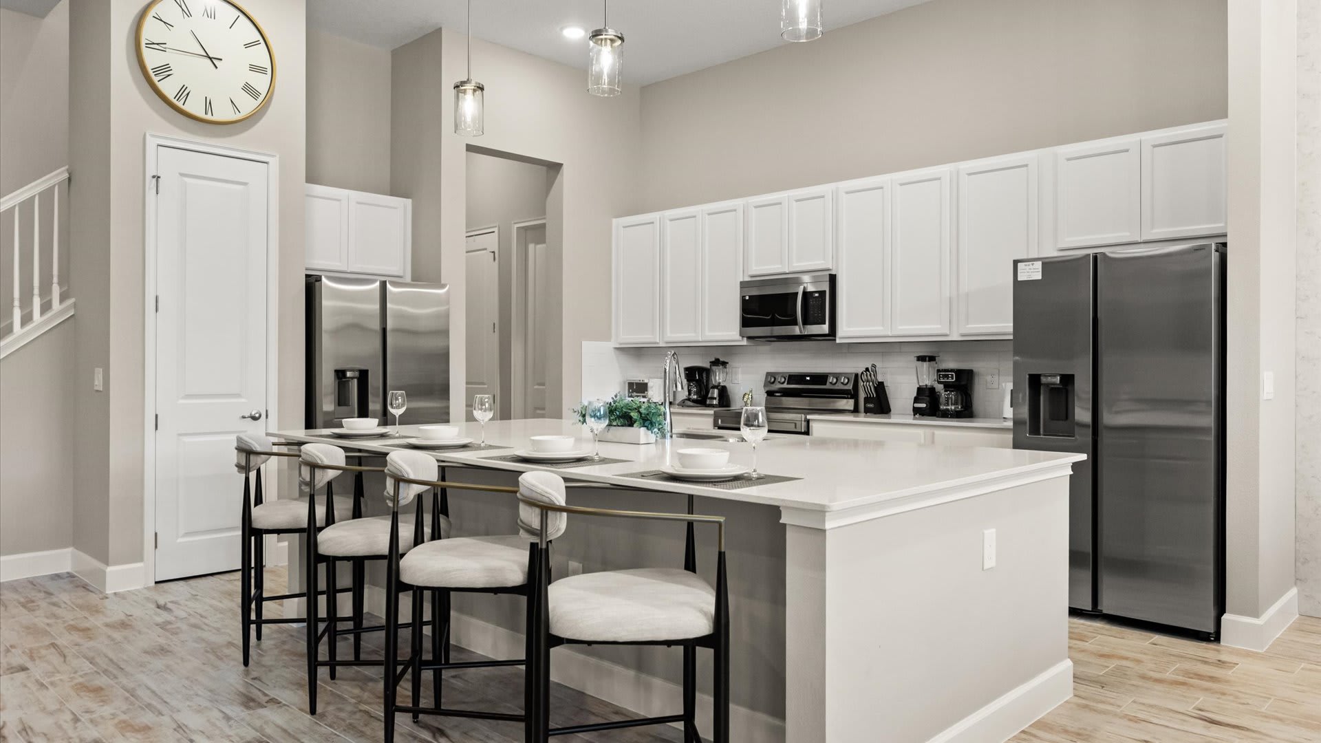 Modern kitchen featuring a large white quartz island with seating for four, equipped with pendant lights overhead. Stainless steel appliances and white cabinetry line the back wall.