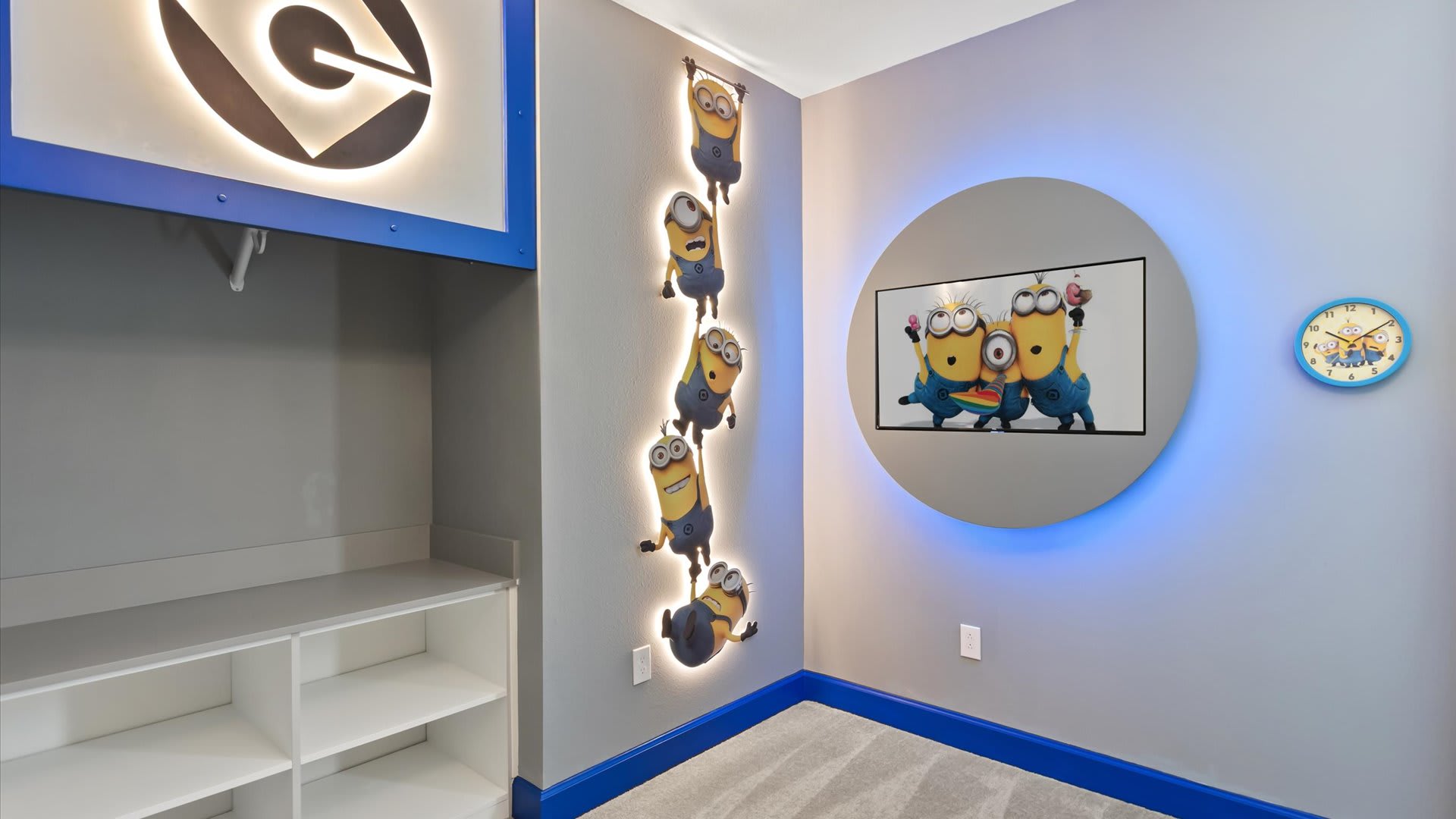 Another view of the 'Minions' themed bedroom, showcasing a built-in closet area with shelves and a large illuminated 'G' logo. A vertical illuminated Minions wall decal is also visible next to the circular TV.