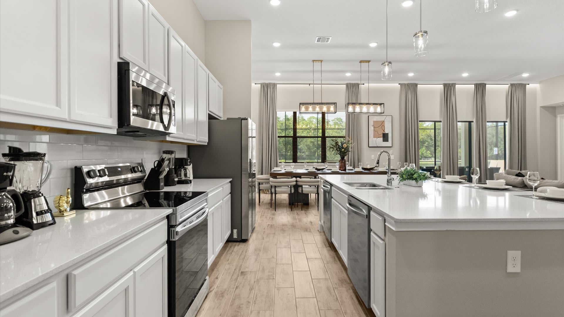 Bright kitchen with white shaker cabinets, white subway tile backsplash, and stainless steel appliances including a range, microwave, and refrigerator. A coffee maker and blender are on the counter.