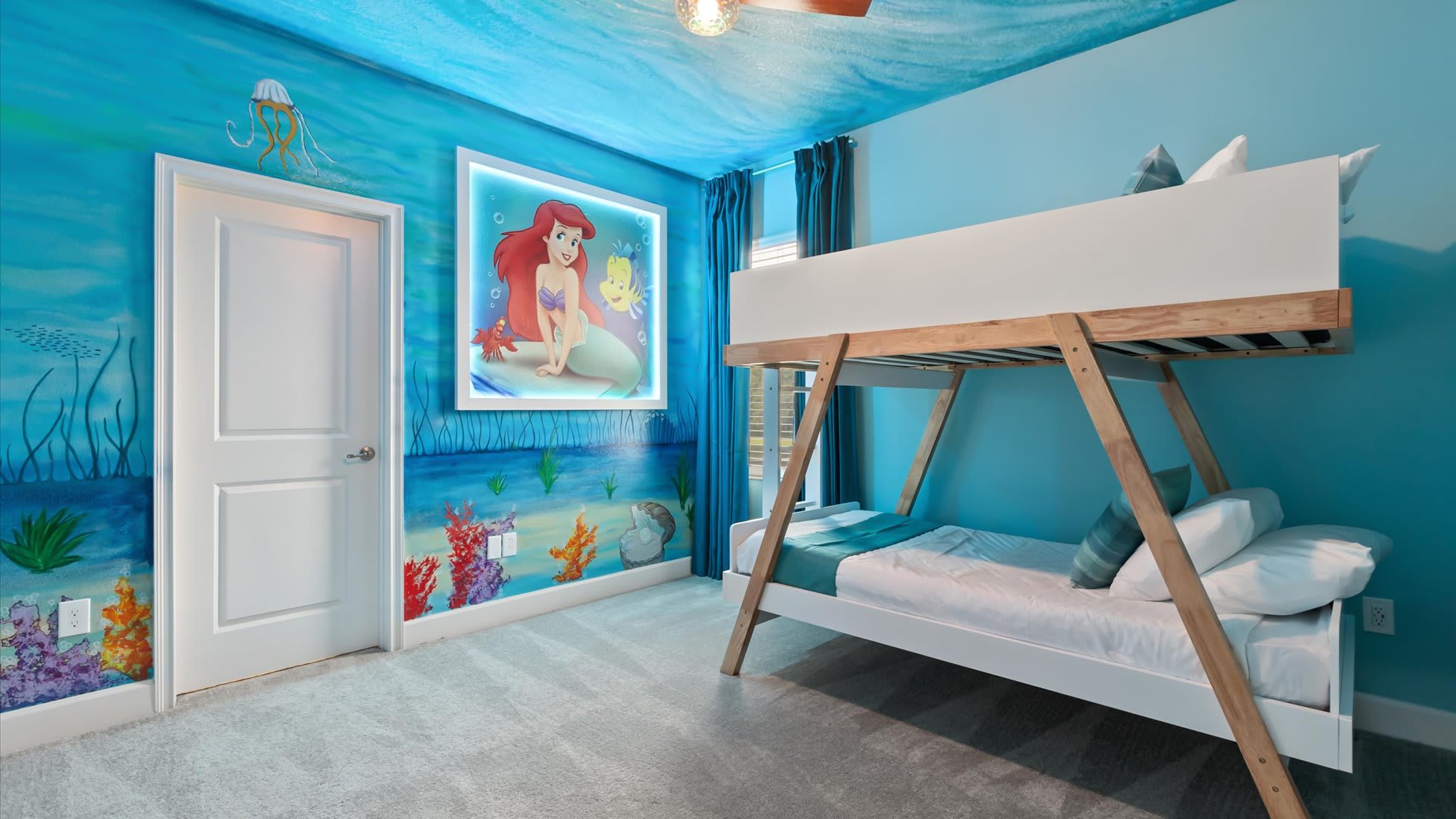 Under the Sea themed bedroom featuring a vibrant blue and green mural depicting Ariel and marine life, complemented by a modern white and wood bunk bed. The ceiling is creatively painted to resemble water.