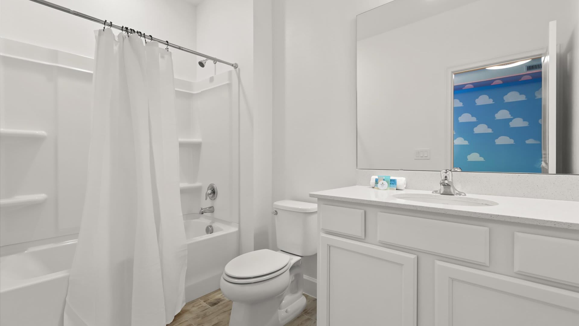 A clean white bathroom features a vanity with a single sink and a large mirror reflecting the 'Toy Story' themed room. It includes a white toilet and a shower/tub combo with a white curtain.