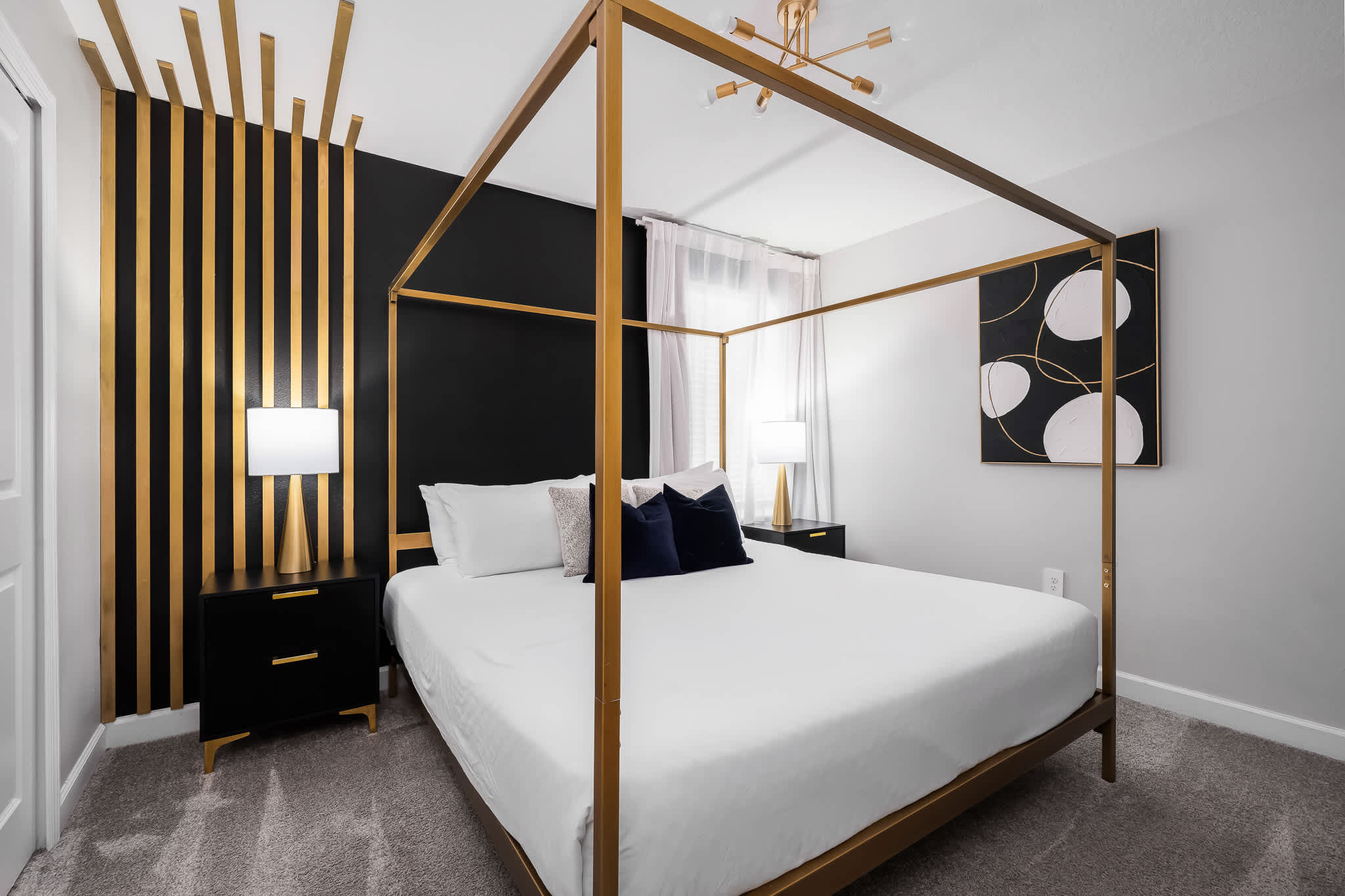 Elegant bedroom featuring a gold four-poster king bed with white bedding and navy accent pillows, set against a striking black accent wall with vertical gold slats, and two black nightstands with gold lamps.