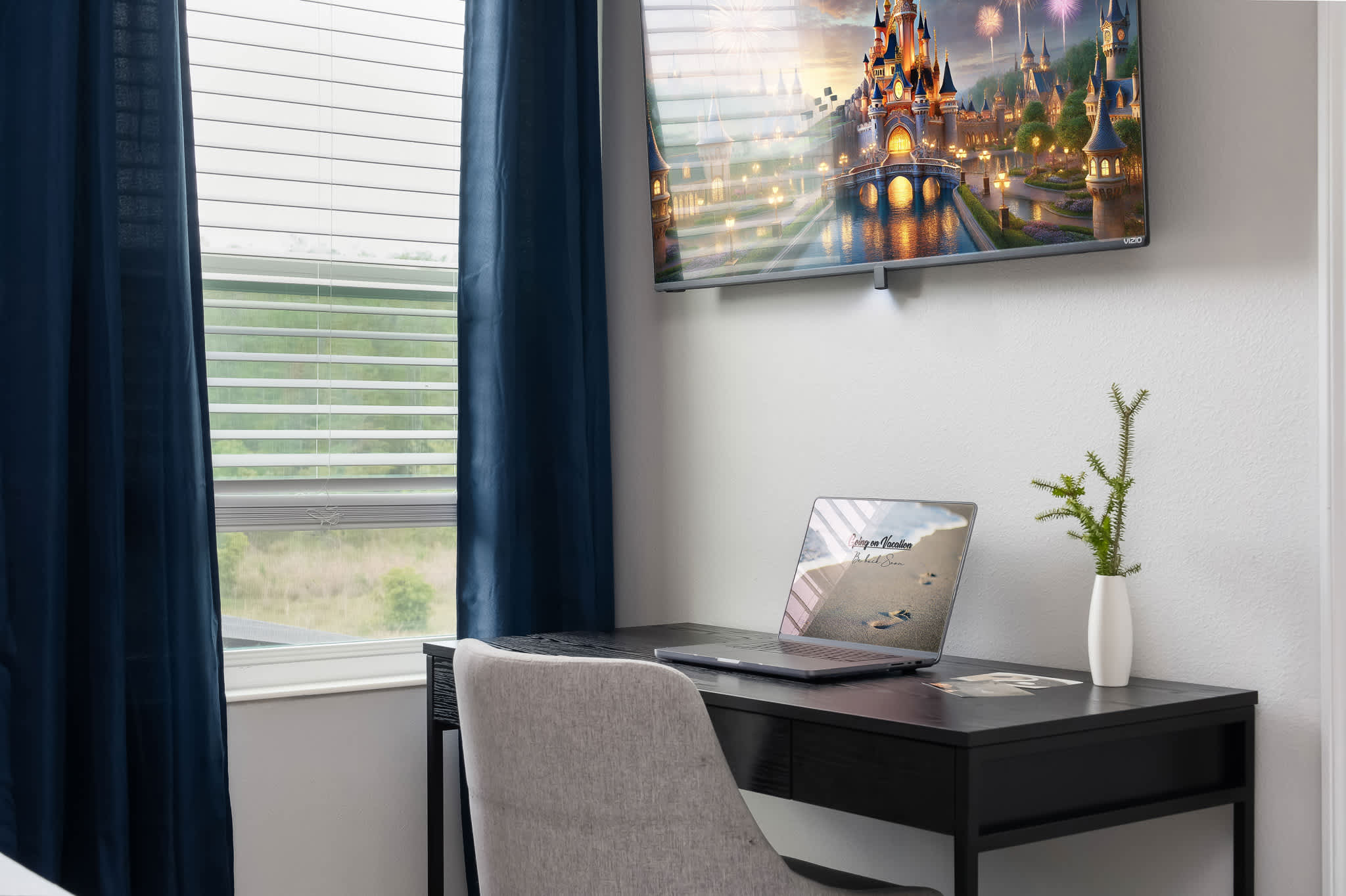 A detailed shot of a black desk with a laptop displaying a beach scene, a white vase with a small plant, and a wall-mounted TV showing a castle, next to a window with blue curtains and blinds.