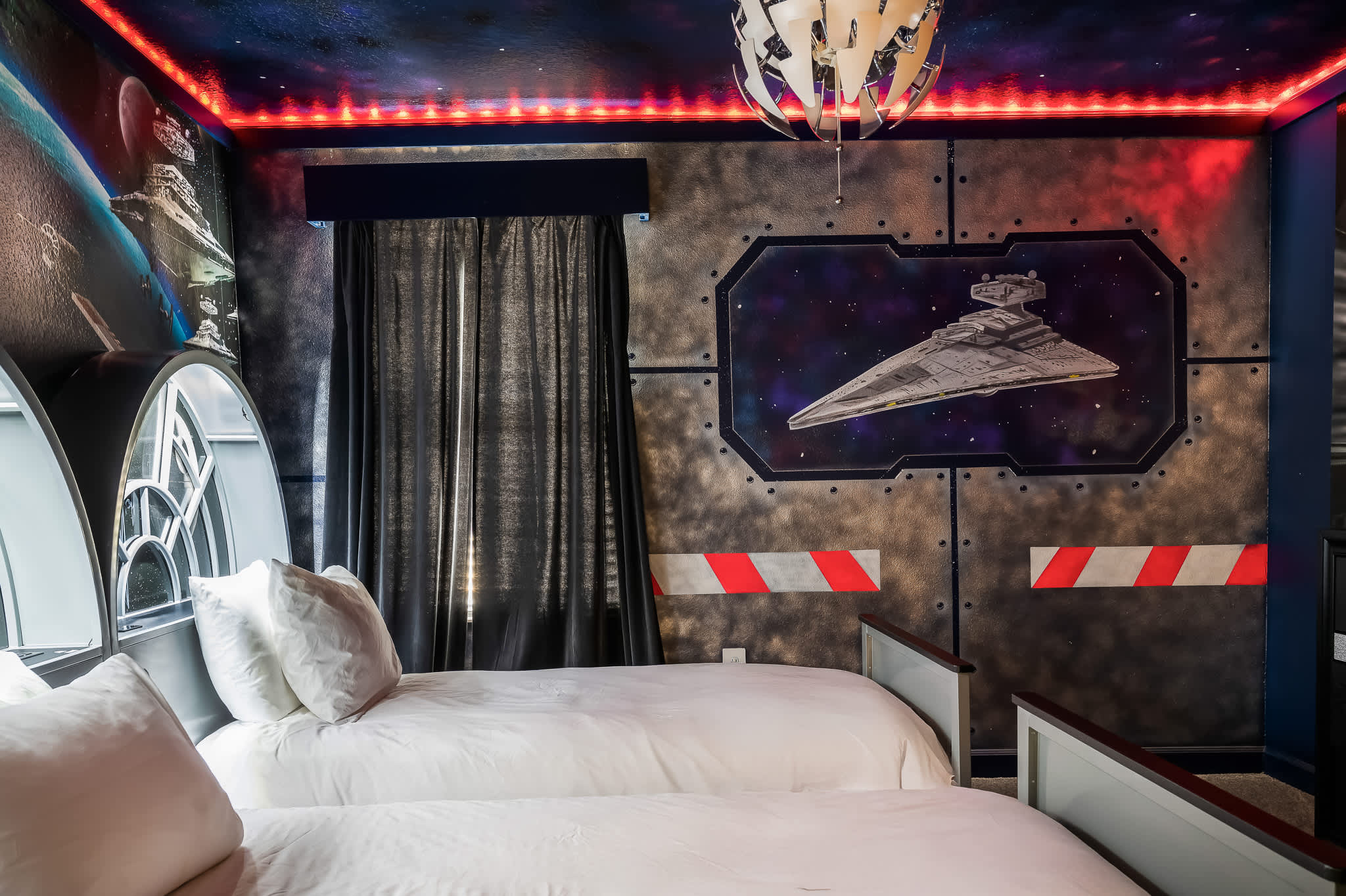Themed bedroom with two twin beds, featuring a dark wall with a Star Destroyer mural and red and white striped accents, dark curtains, and a starry ceiling with red LED lighting.