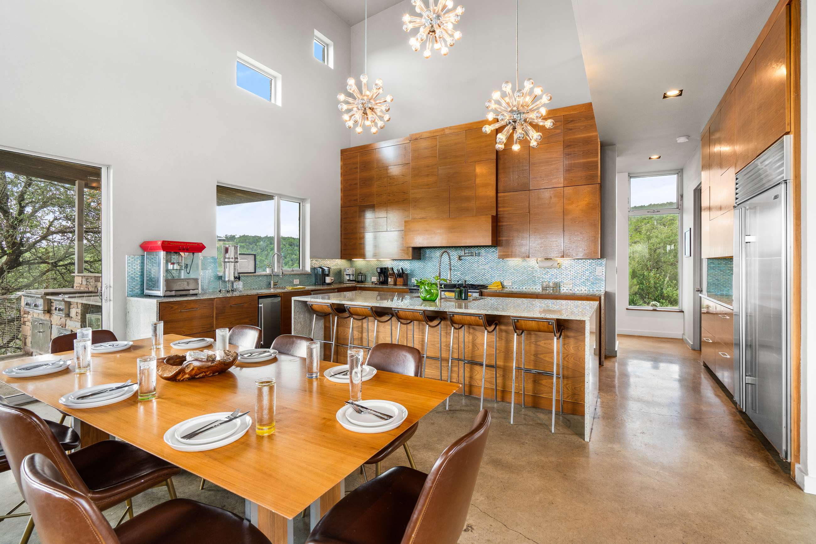 Spacious kitchen with warm wooden cabinetry, light granite countertops, and a blue mosaic tile backsplash, featuring a large island with bar seating and an adjacent dining table.
