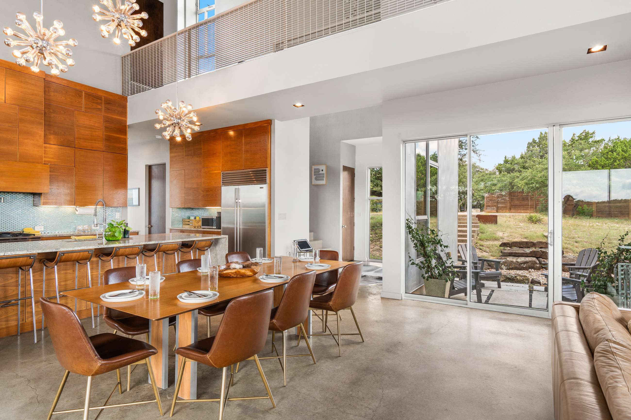 Dining area with a wooden table and leather chairs, looking towards a modern kitchen with wooden cabinets and a large stainless steel refrigerator, and an adjacent entryway with outdoor access.