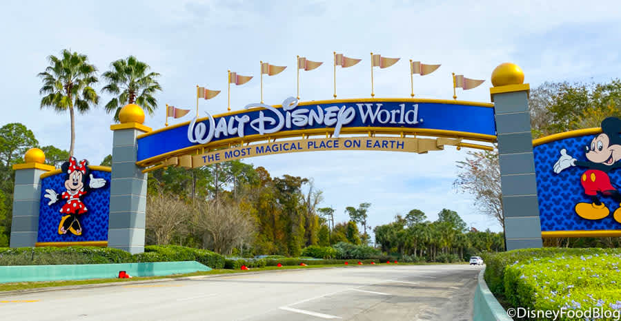 Grand entrance sign for Walt Disney World, featuring a blue archway with "THE MOST MAGICAL PLACE ON EARTH" text, adorned with Mickey and Minnie Mouse characters and golden globes, under a bright sky.