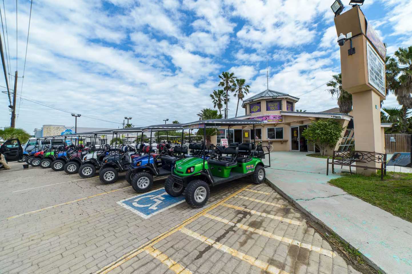 Outdoor parking lot filled with numerous golf carts available for rent, parked in front of a commercial building with palm trees under a bright blue sky.