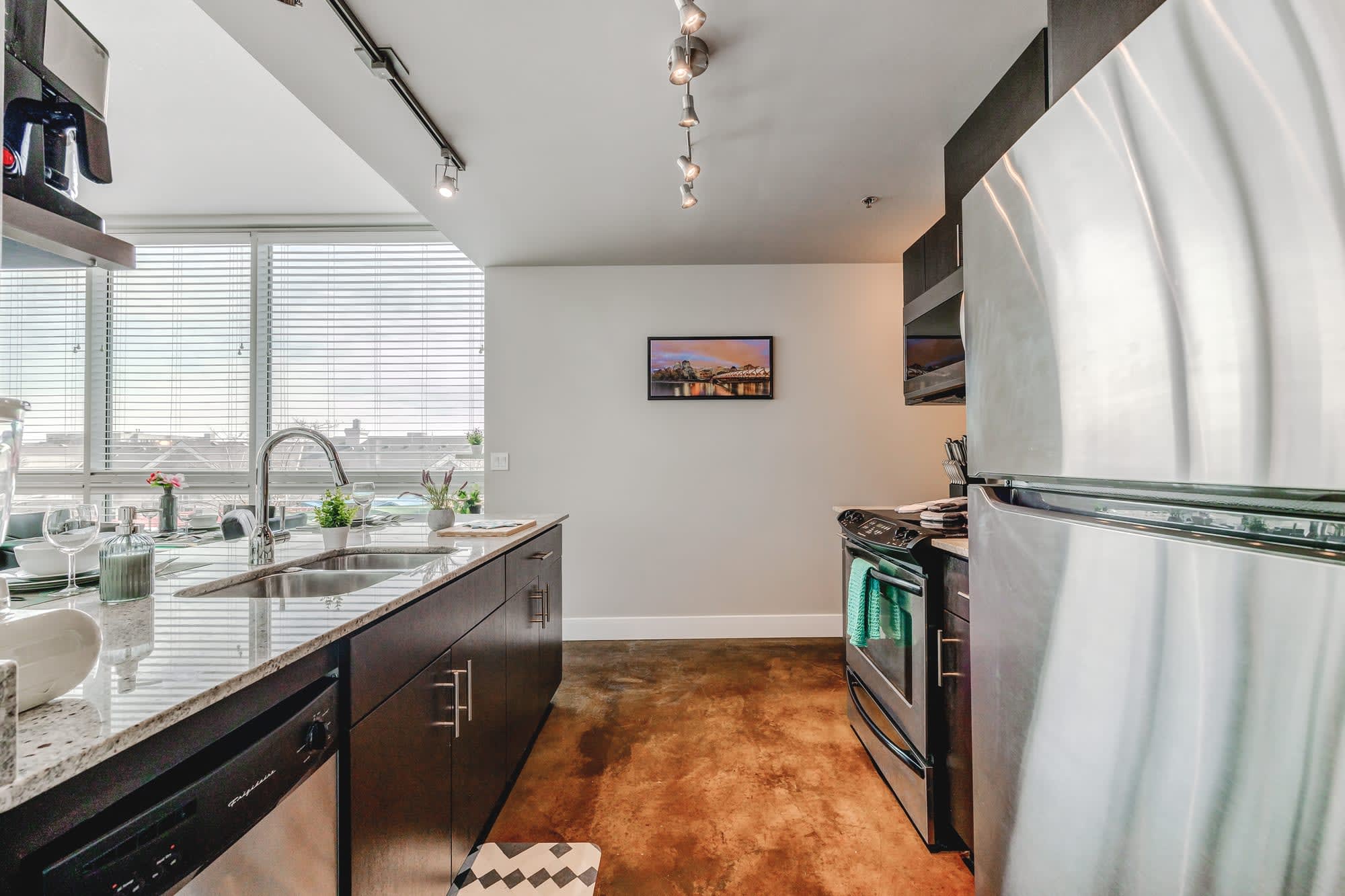 Contemporary kitchen view highlighting a stainless steel refrigerator and stove, dark cabinetry, and granite countertops. A small wall-mounted television is visible above the counter.