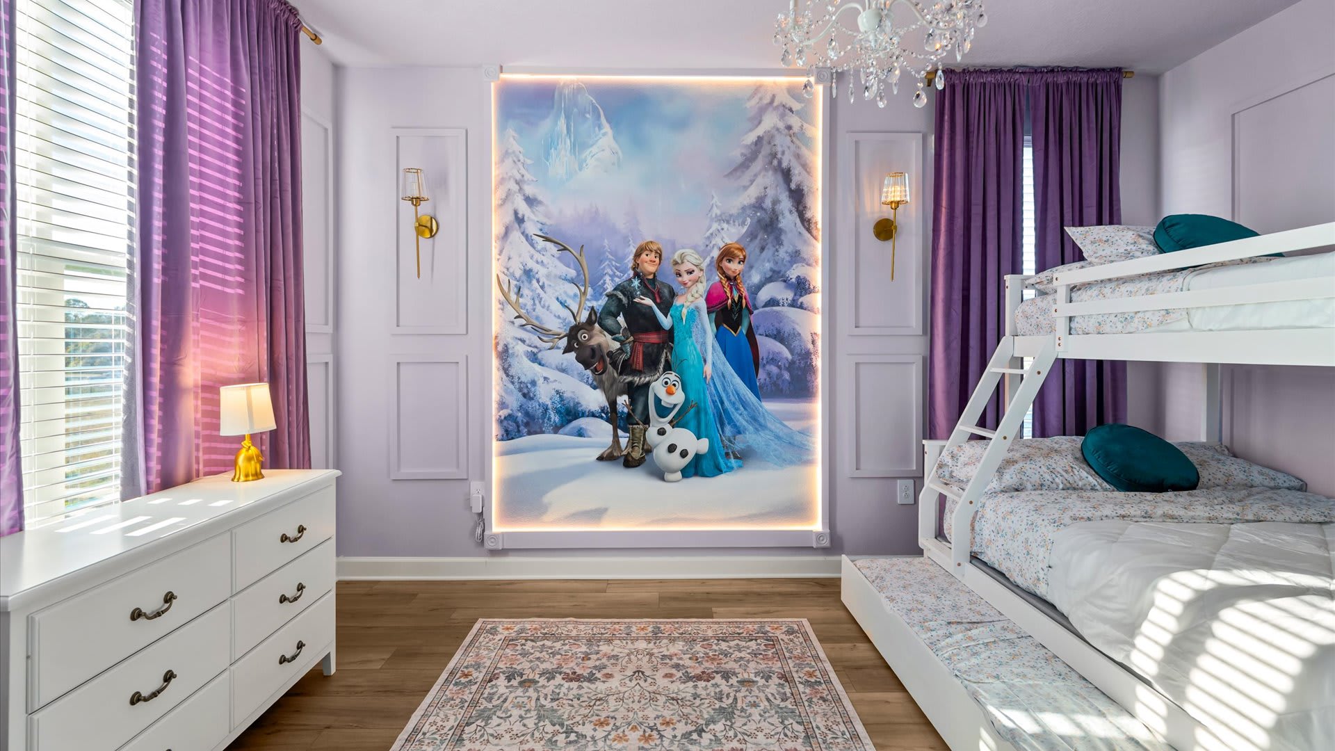 The kids' bedroom features white bunk beds and a large illuminated mural of Disney's Frozen characters on the wall. Light purple walls with decorative paneling, purple curtains, and a white dresser are also visible.