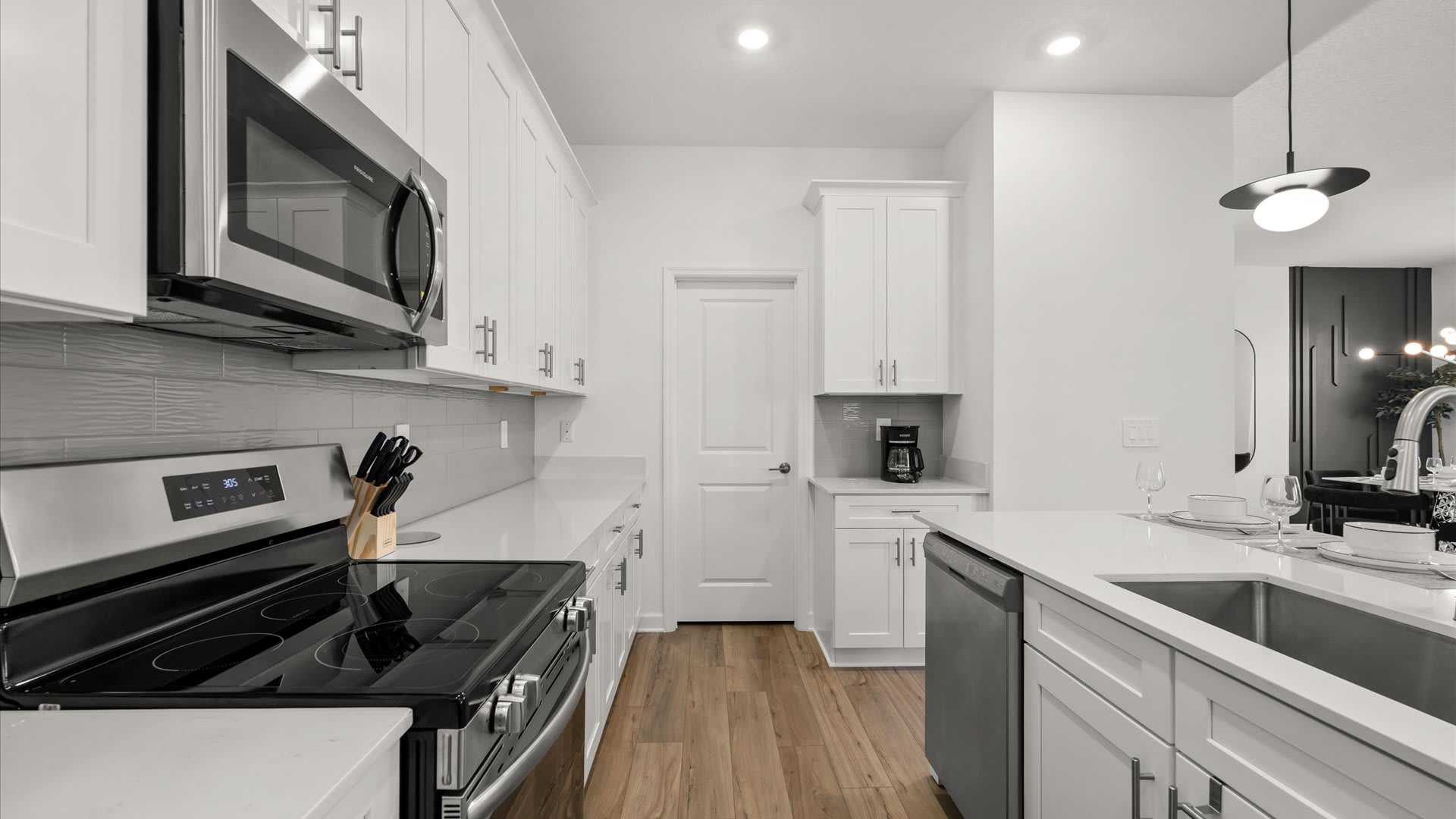 Modern kitchen counter with white quartz countertops, a stainless steel electric range, microwave, and a grey subway tile backsplash, featuring white shaker cabinets and a coffee maker in the corner.