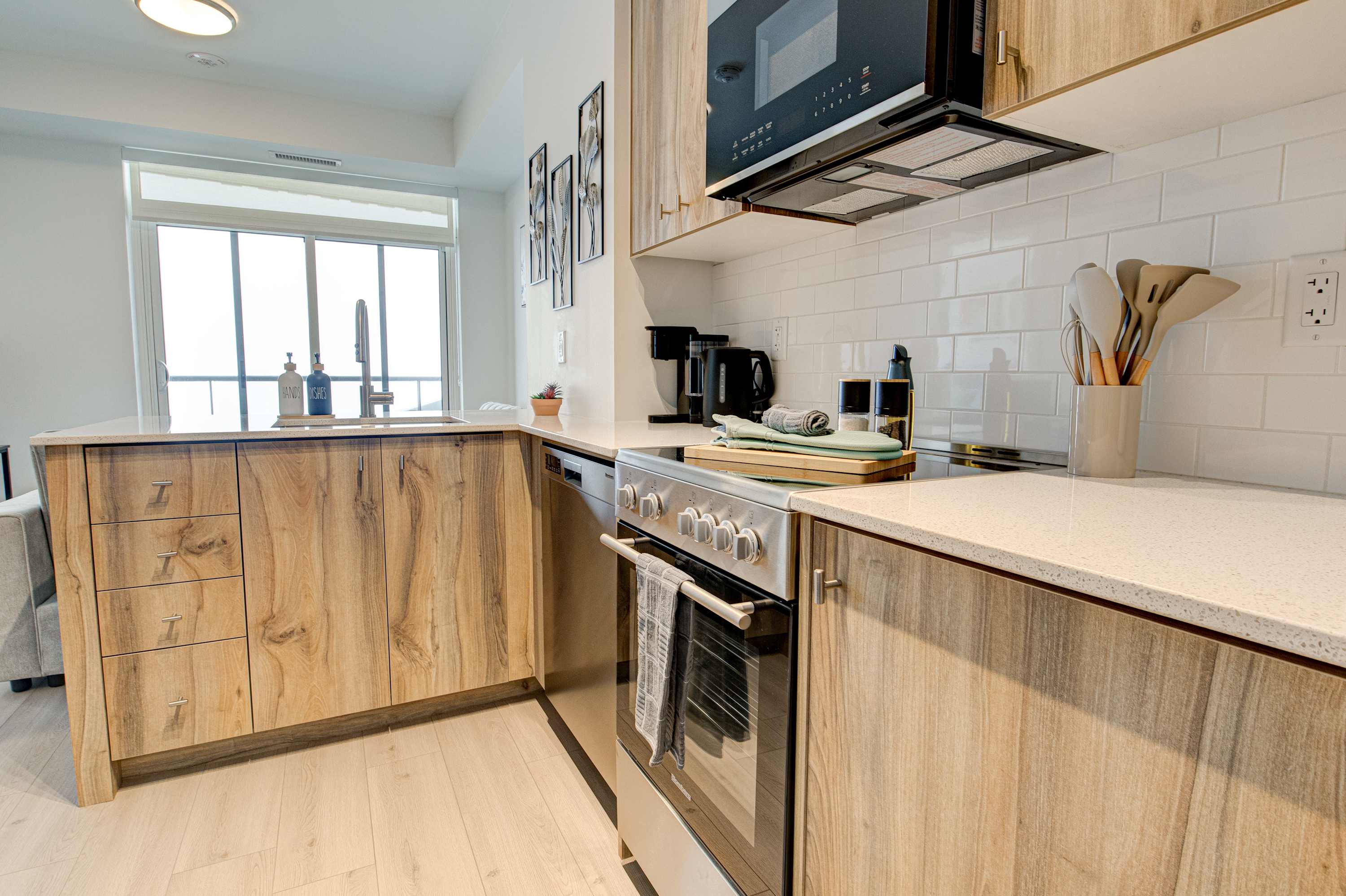 Detailed view of the modern kitchen showcasing light wood cabinetry, white quartz countertops, a stainless steel sink with a gooseneck faucet, and an electric stove with an oven.