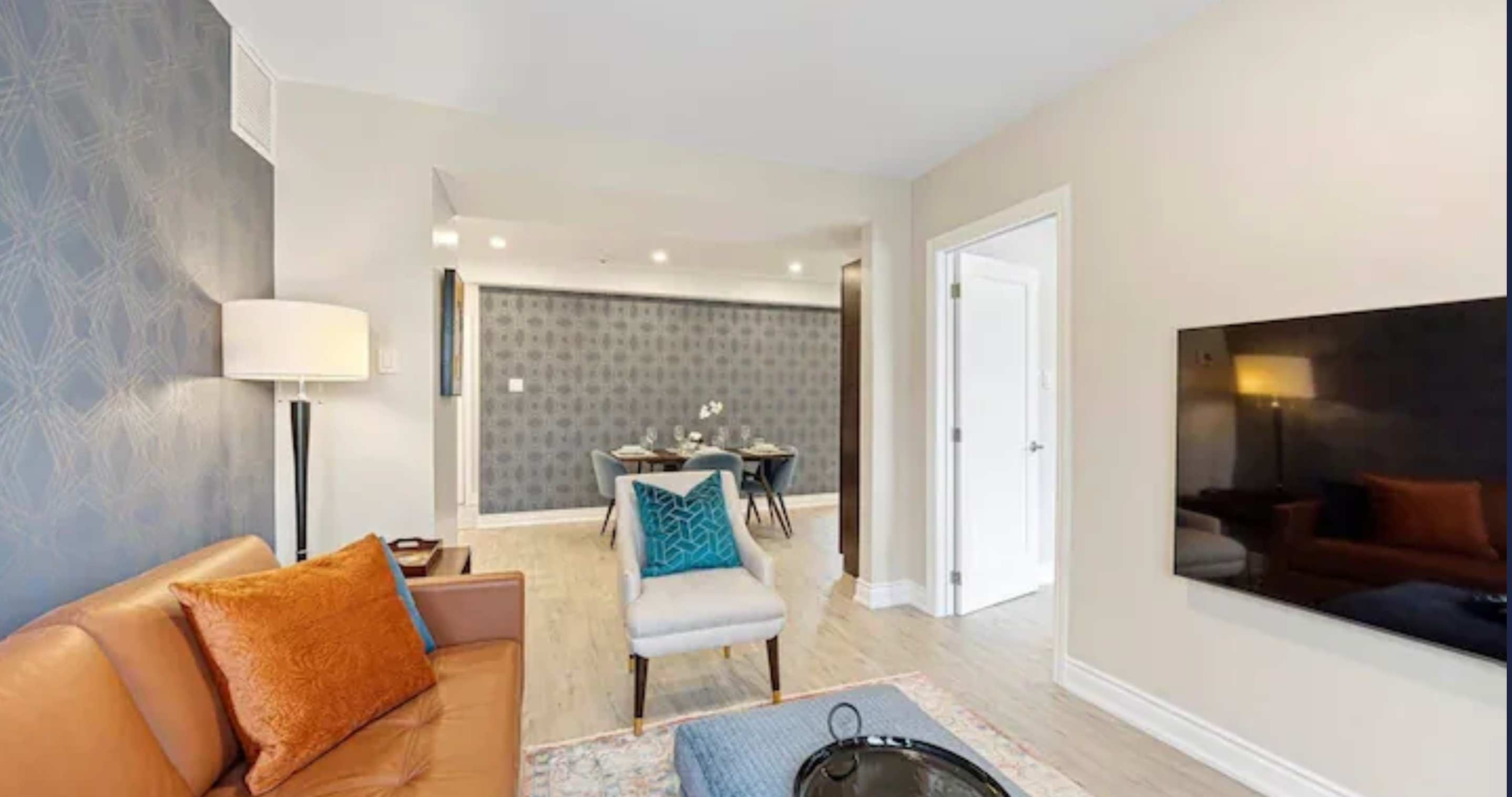 A view from the living room towards the dining area, showcasing the tan leather sofa, a cream armchair, and the patterned accent wall that extends into the dining space.