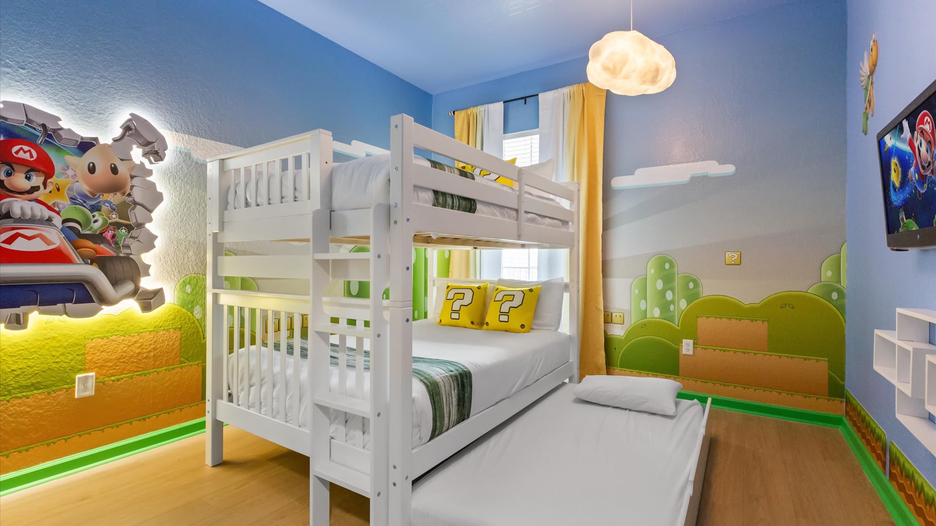 A vibrant Super Mario themed bedroom featuring a white bunk bed with a trundle, blue walls with game-inspired murals, and a cloud-shaped ceiling light. A large Mario wall art piece is illuminated.