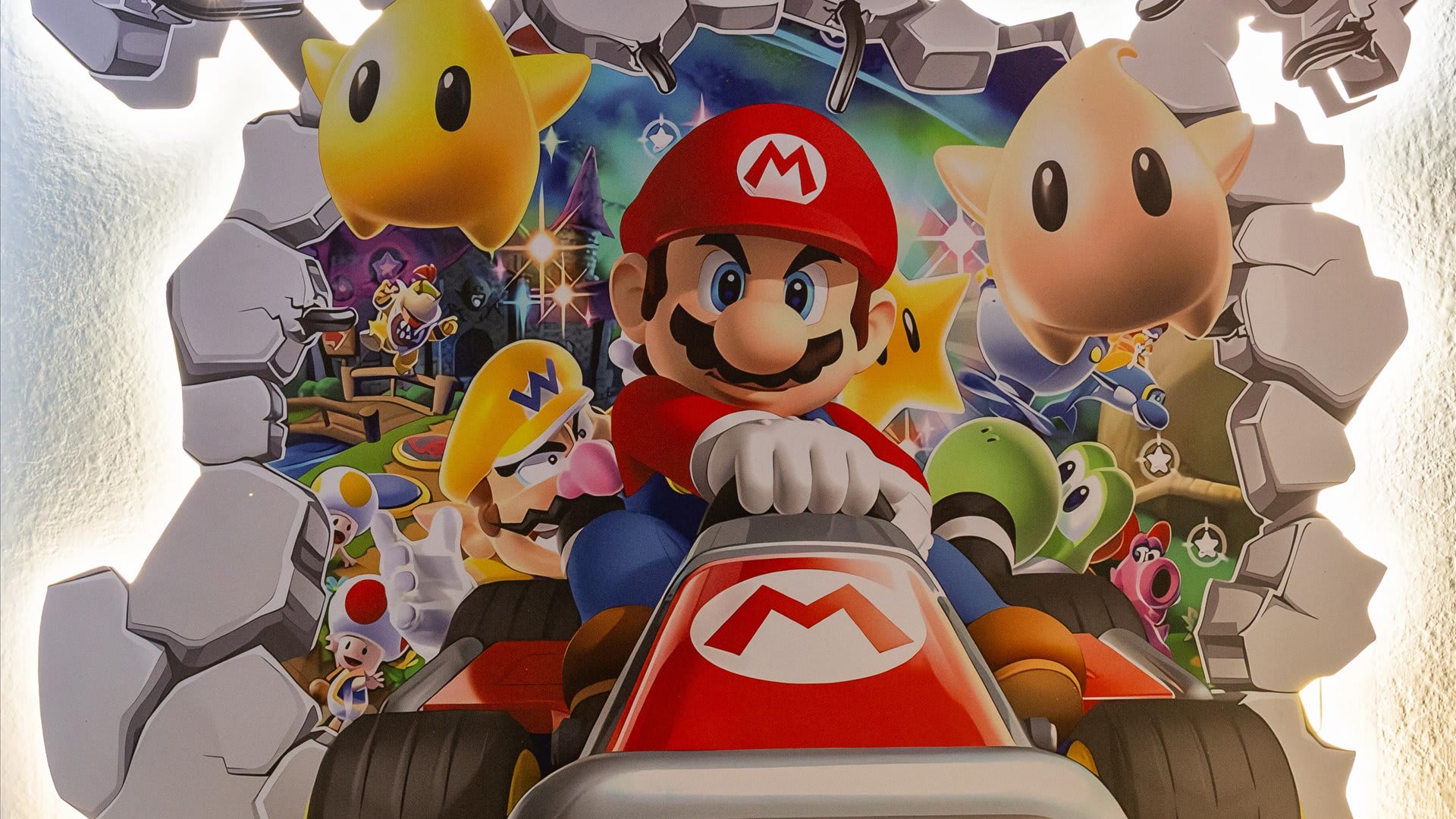 A detailed close-up of the illuminated Super Mario wall art, depicting Mario in a kart surrounded by other characters and stars, breaking through a wall.