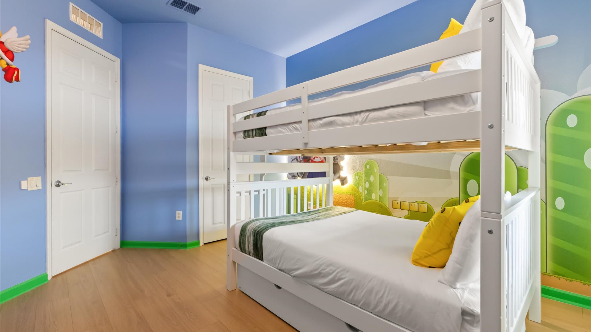 Themed kids' bedroom with light blue walls and a white bunk bed featuring a full-size bottom and twin top, adorned with yellow pillows and Mario-themed wall decals.