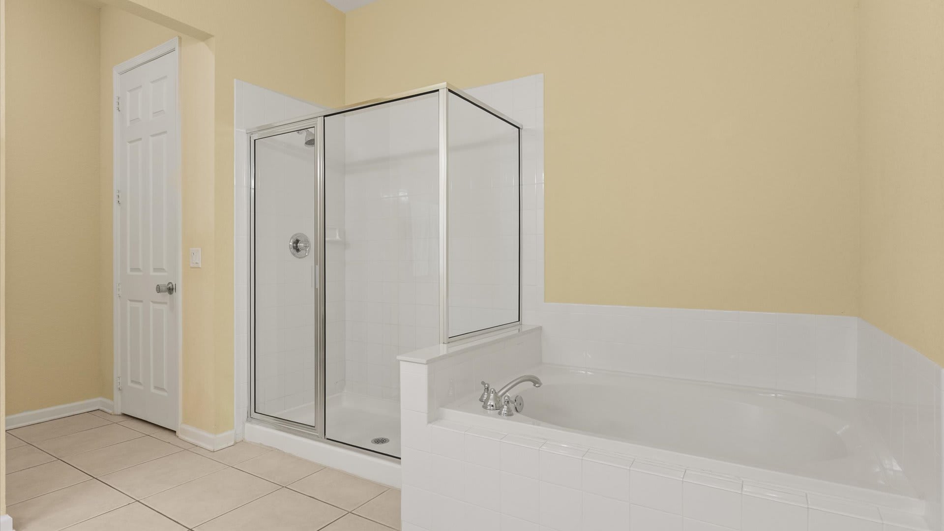 A section of the bathroom showcasing a white tiled built-in bathtub with chrome fixtures and a separate glass-enclosed shower stall. The walls are painted a soft yellow.