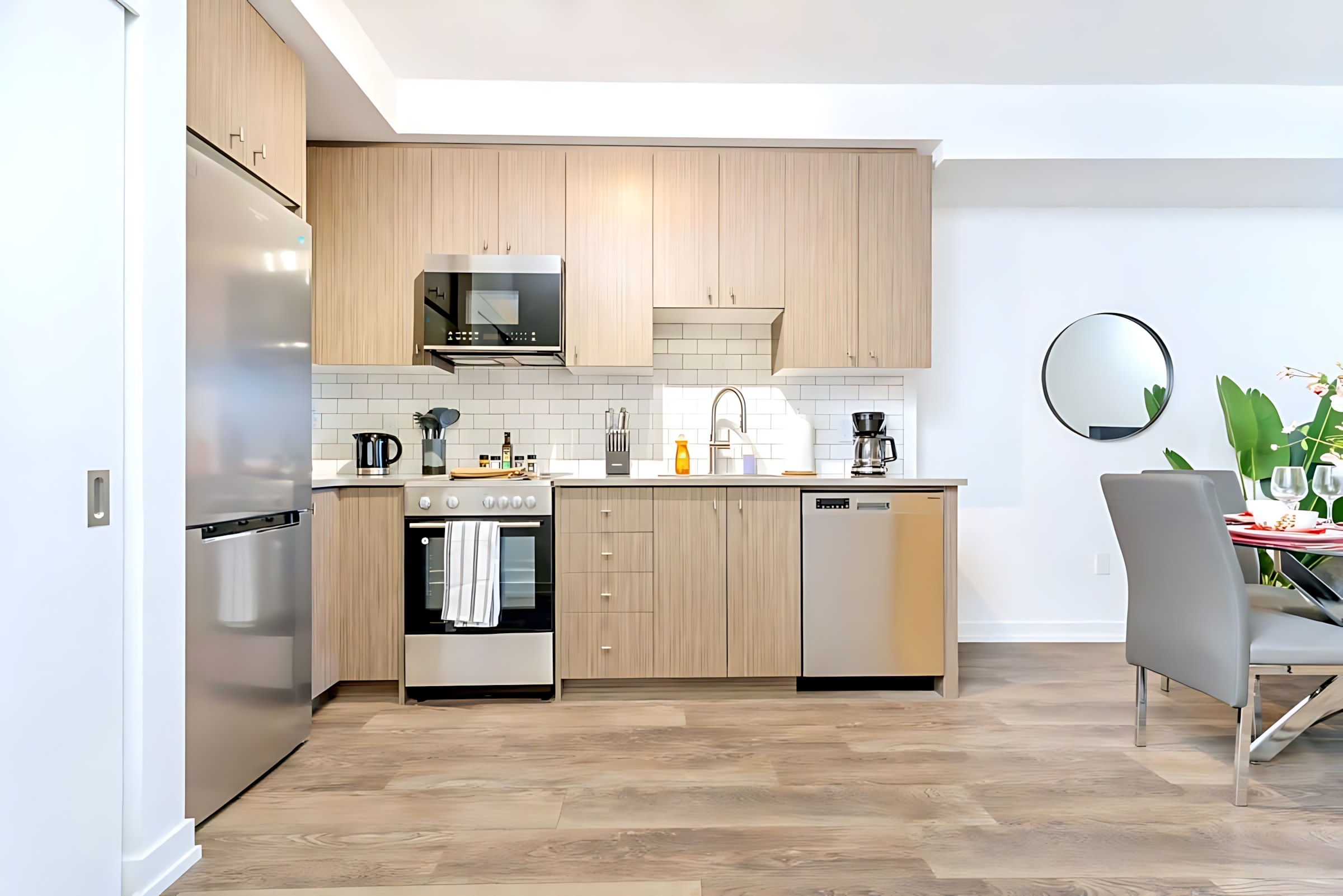 Spacious modern kitchen featuring light wood cabinetry, stainless steel appliances, white subway tile backsplash, and a large refrigerator, with hardwood floors extending into the open-concept living space.